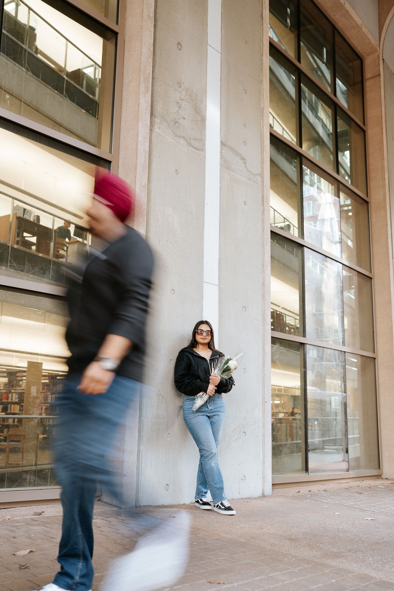 Motion blur captures people walking past a modern building exterior with white columns and glass windows.