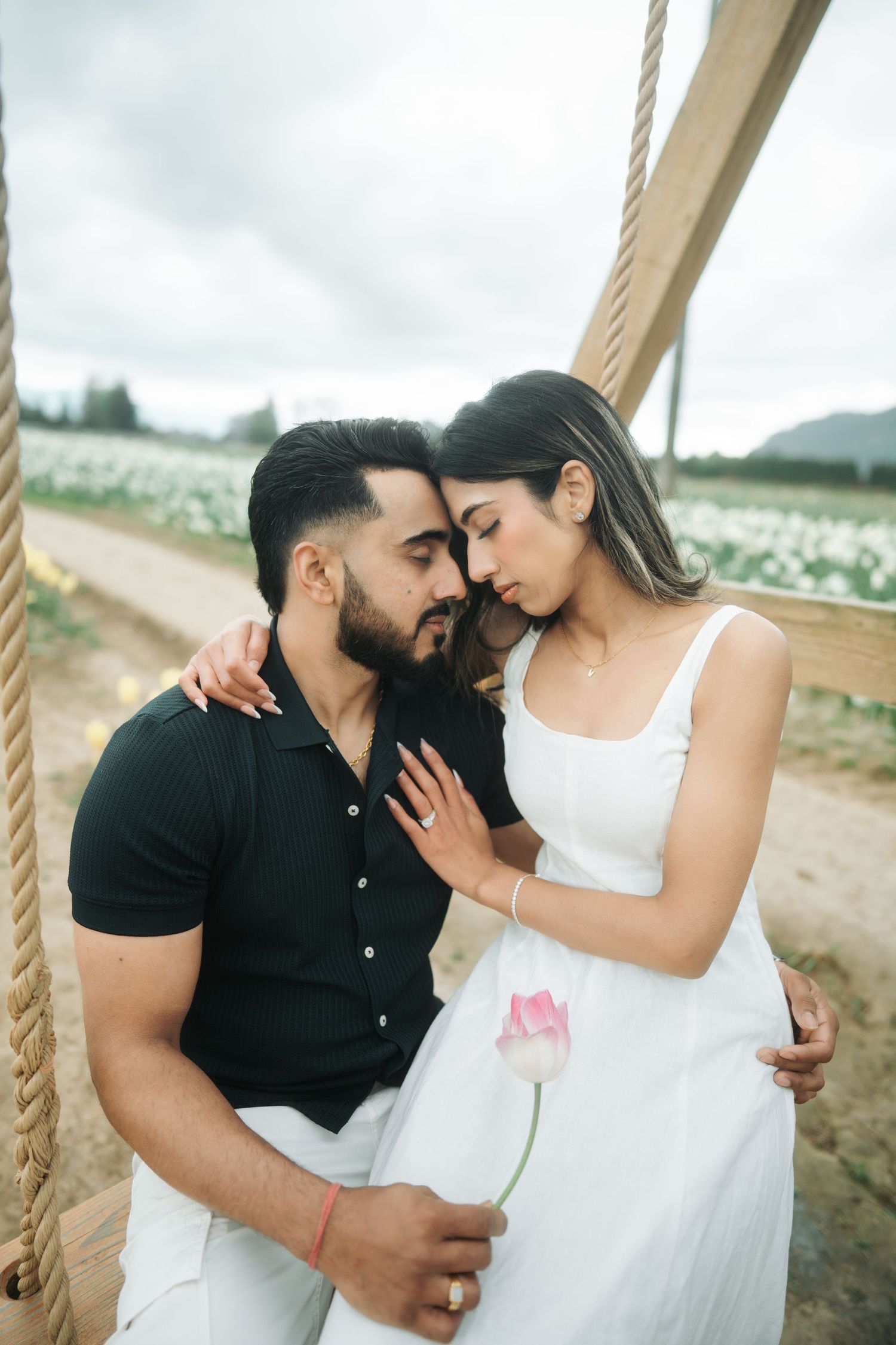 Romantic couple embraces on beach swing in series of intimate engagement photos.