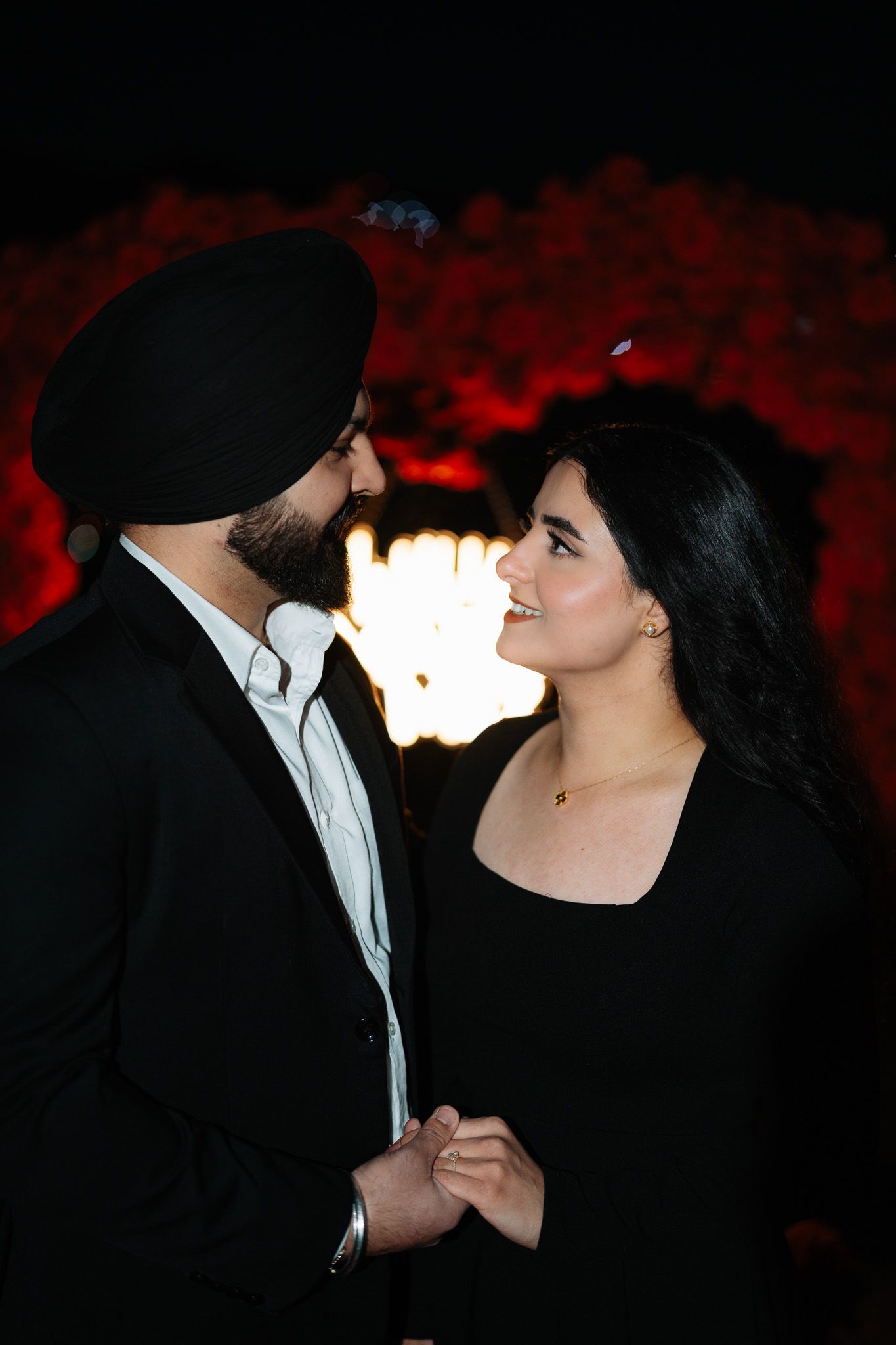 A romantic silhouette of a couple in formal attire gazing at each other against a dark red background.