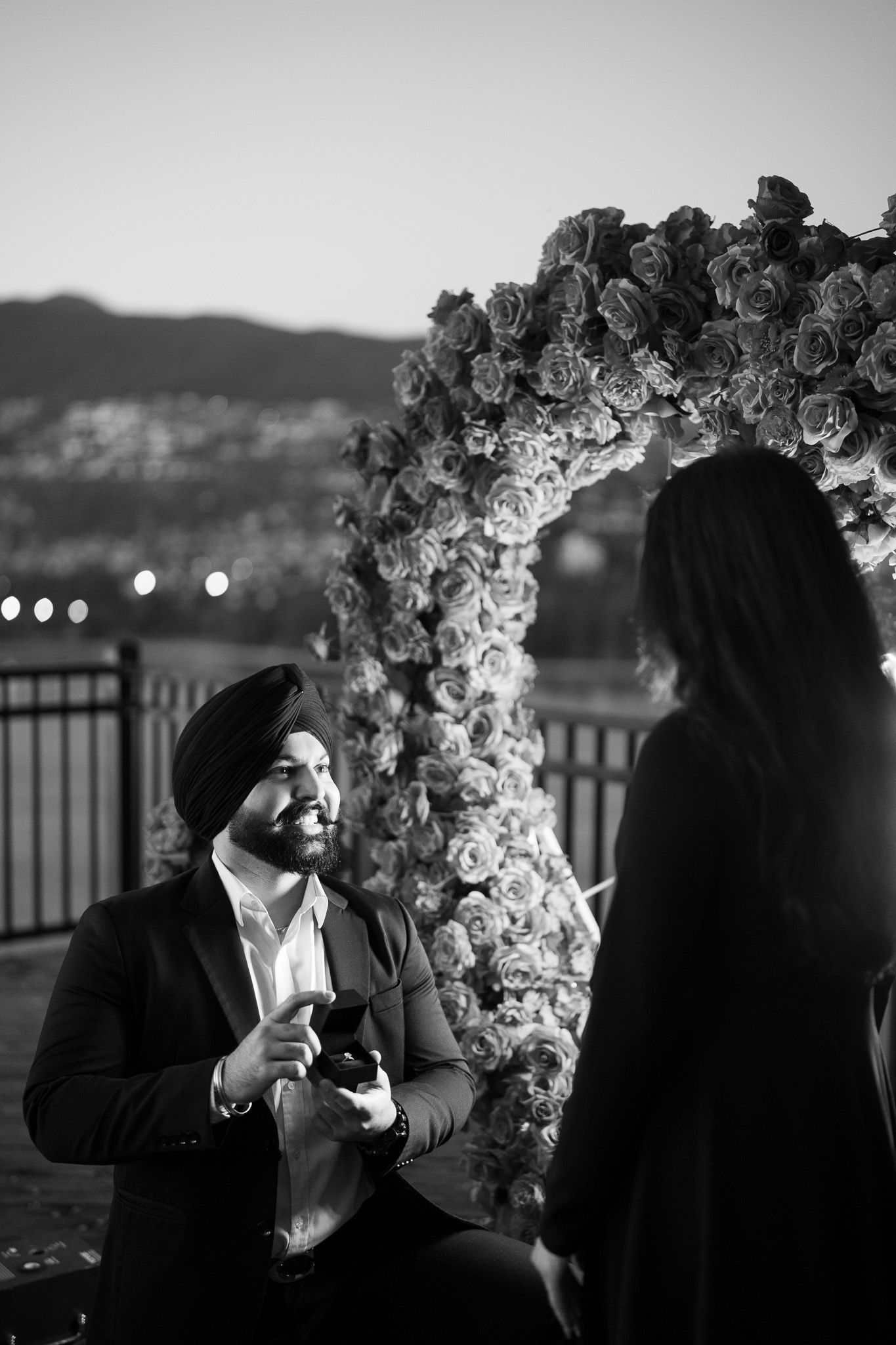 A romantic couple shares an intimate moment under a floral arch during sunset at an outdoor venue.