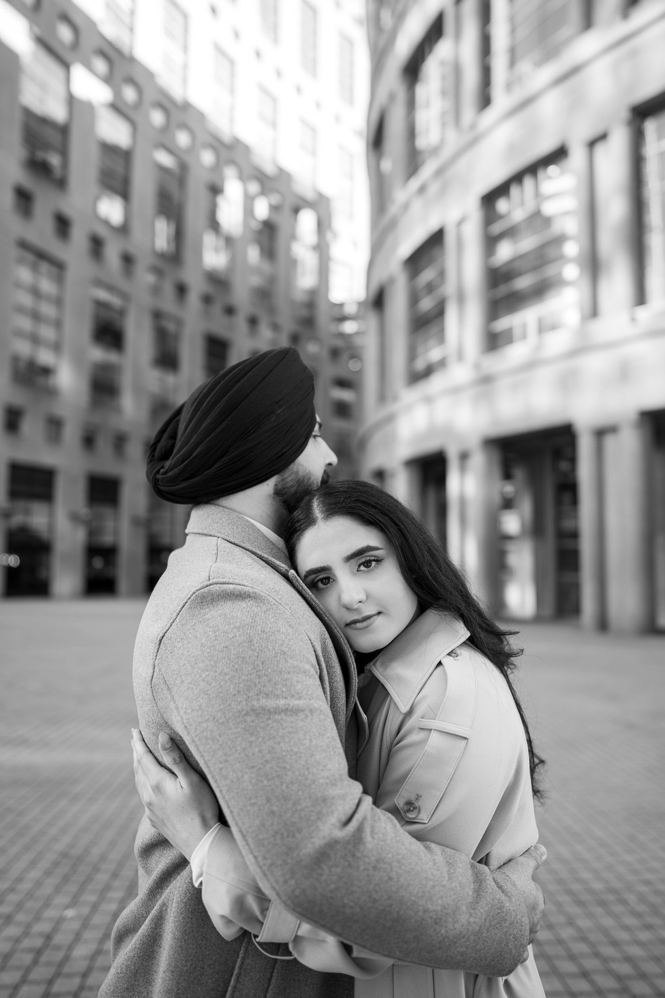 A romantic black and white photo series showing a couple embracing on a city street with modern buildings in the background.