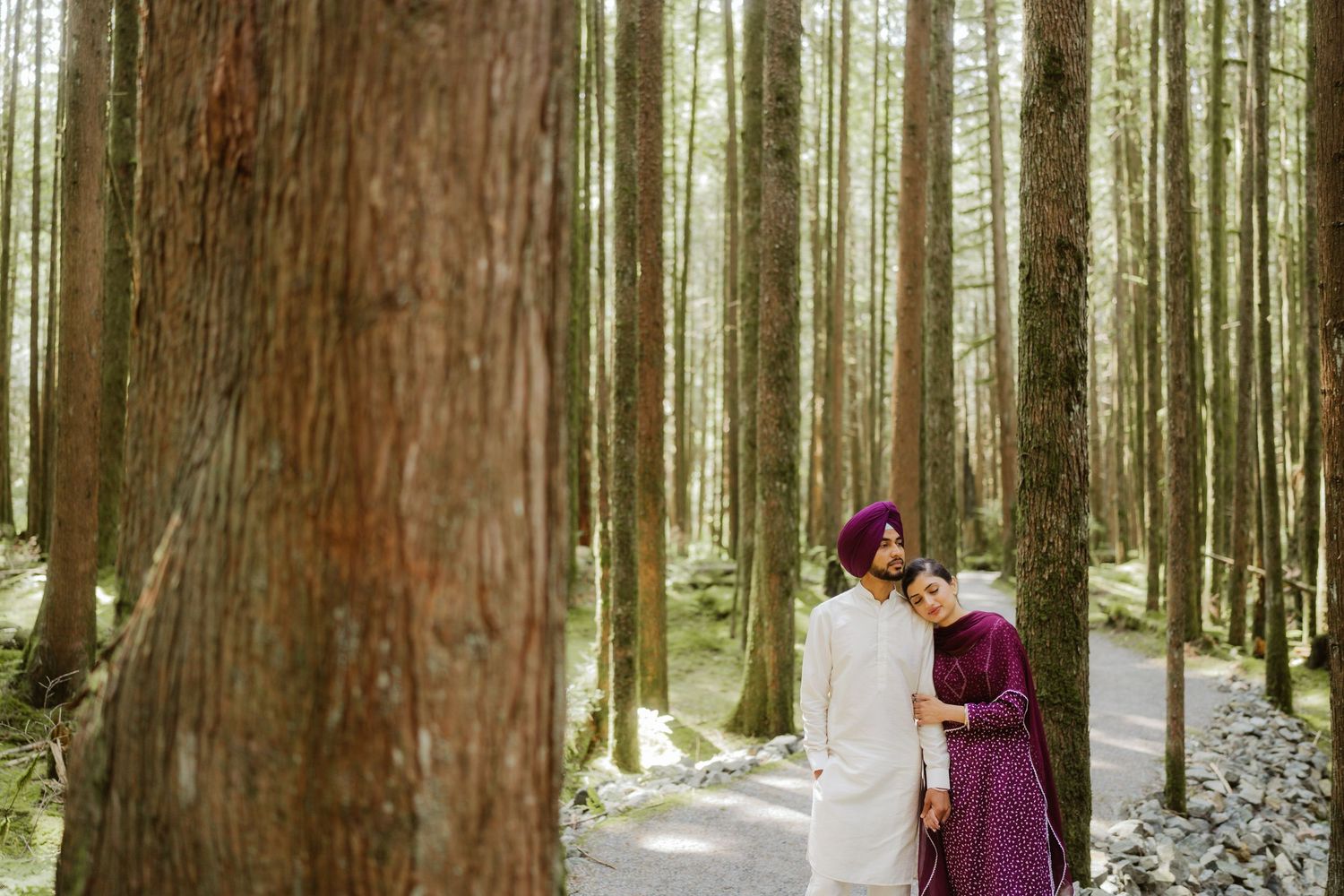 Sikh couple in traditional attire embracing among tall trees in a serene forest setting.