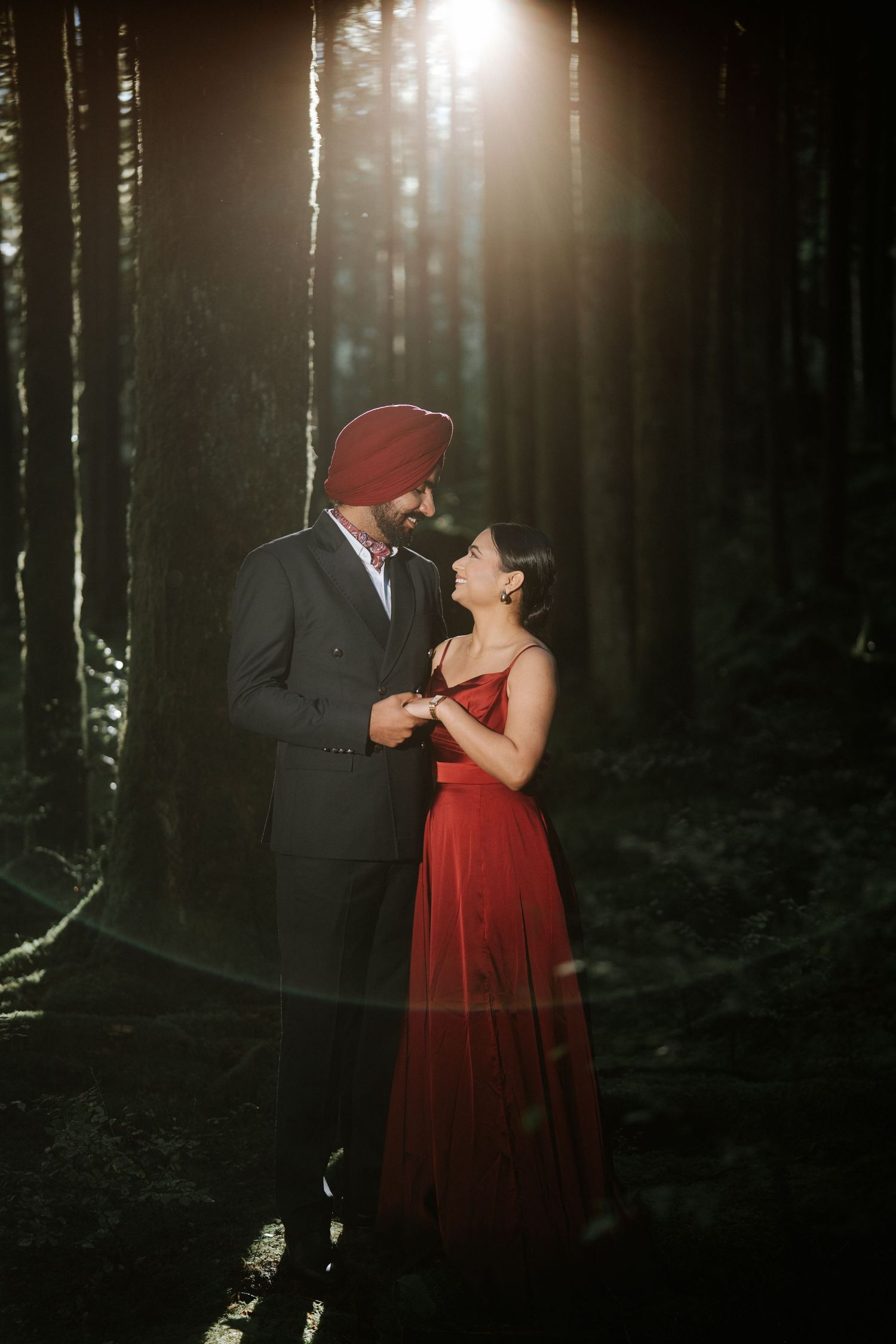 Romantic forest photoshoot featuring a couple in formal wear with sunlight filtering through trees.