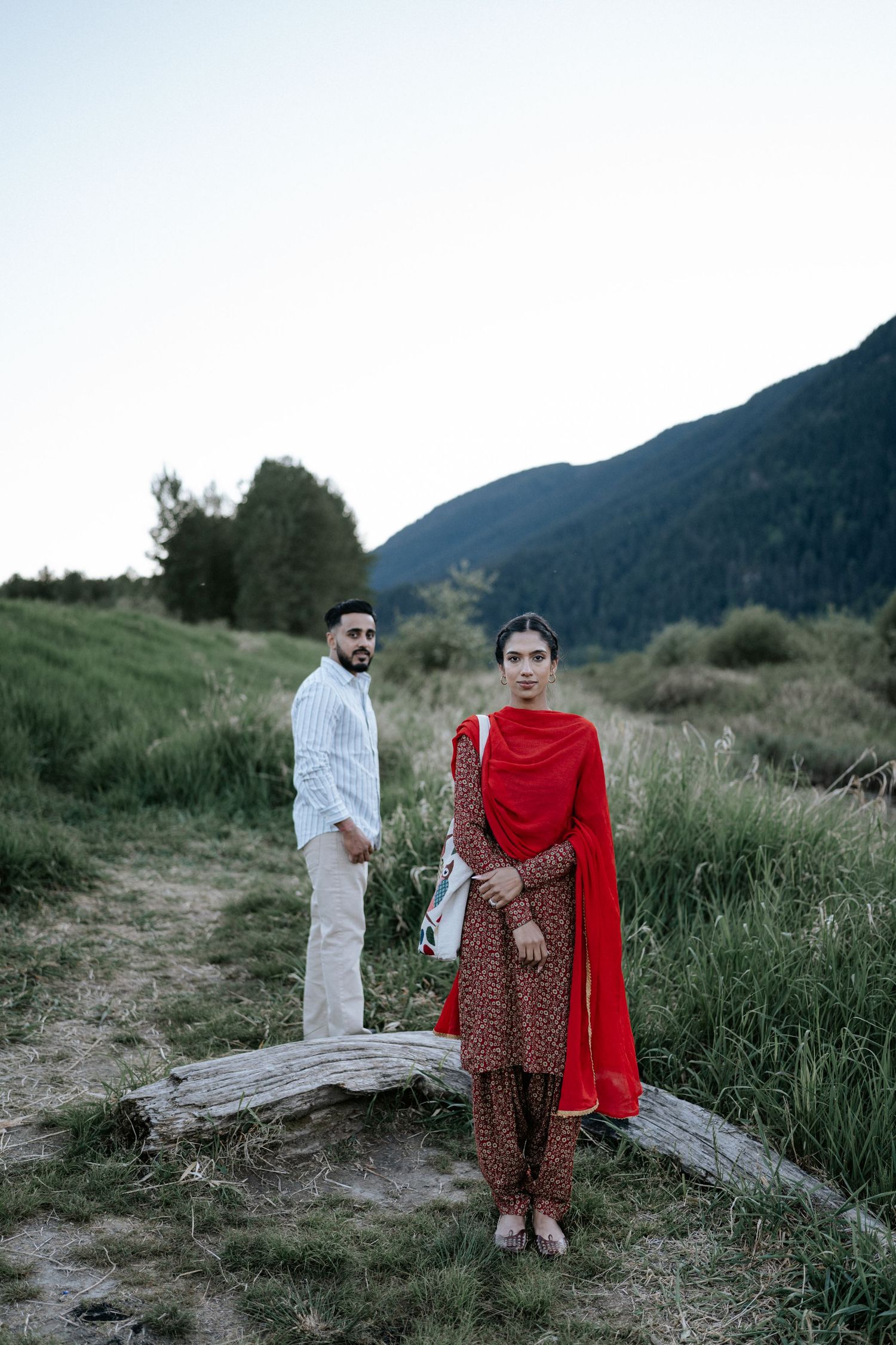 A couple in traditional South Asian attire walks along a mountain trail during golden hour.