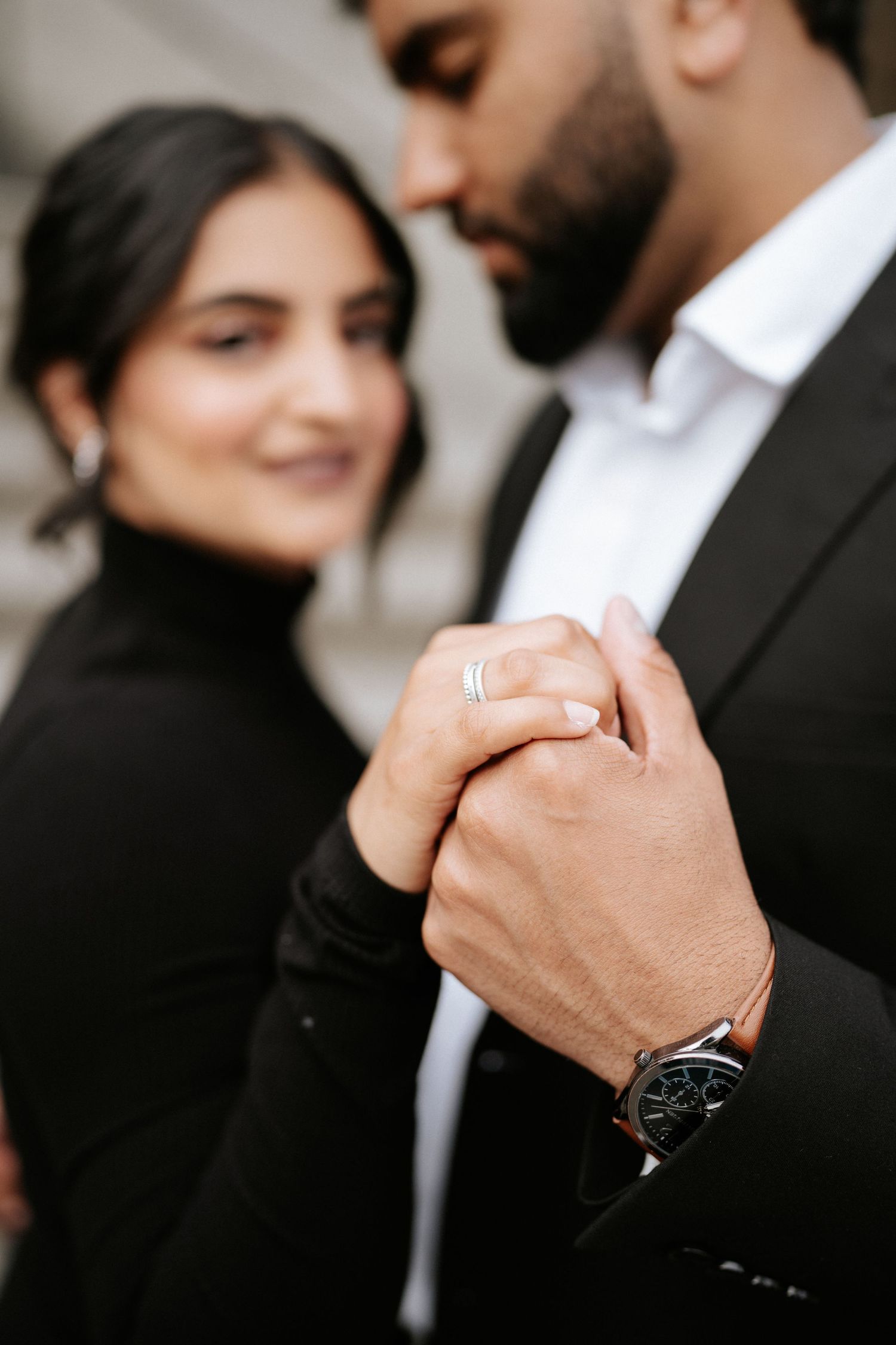 A close-up shot of clasped hands showing wedding rings and a black watch.