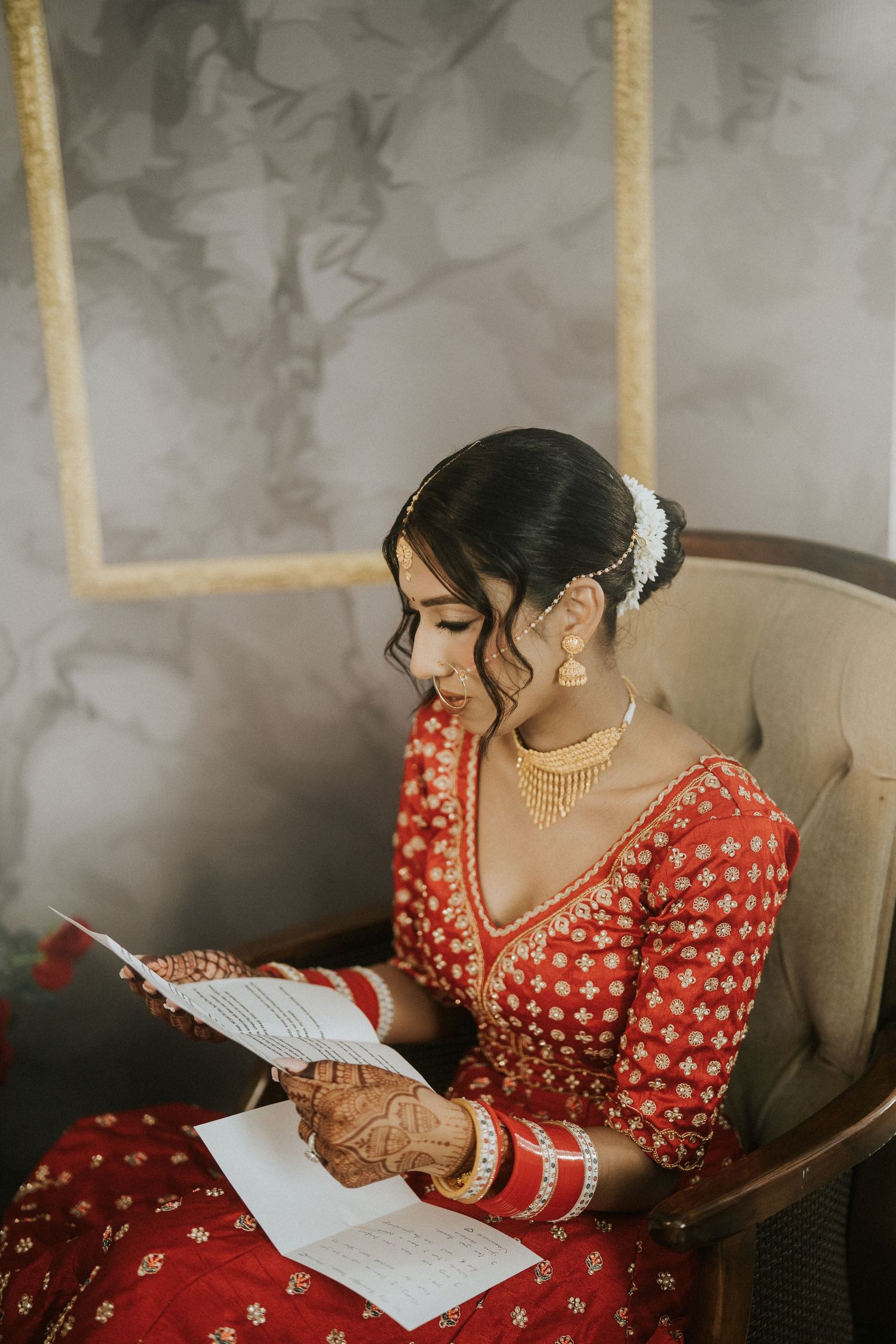 Bride in red embroidered lehenga reads handwritten notes in a beautifully decorated room.