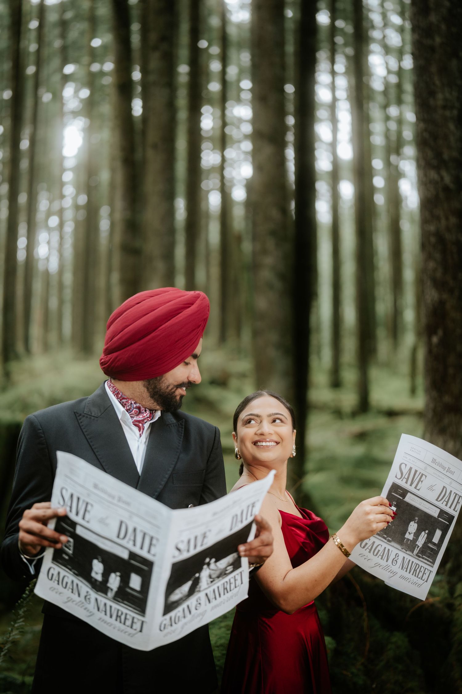 Couple in formal wear shares playful moments with newspapers in a lush forest setting.