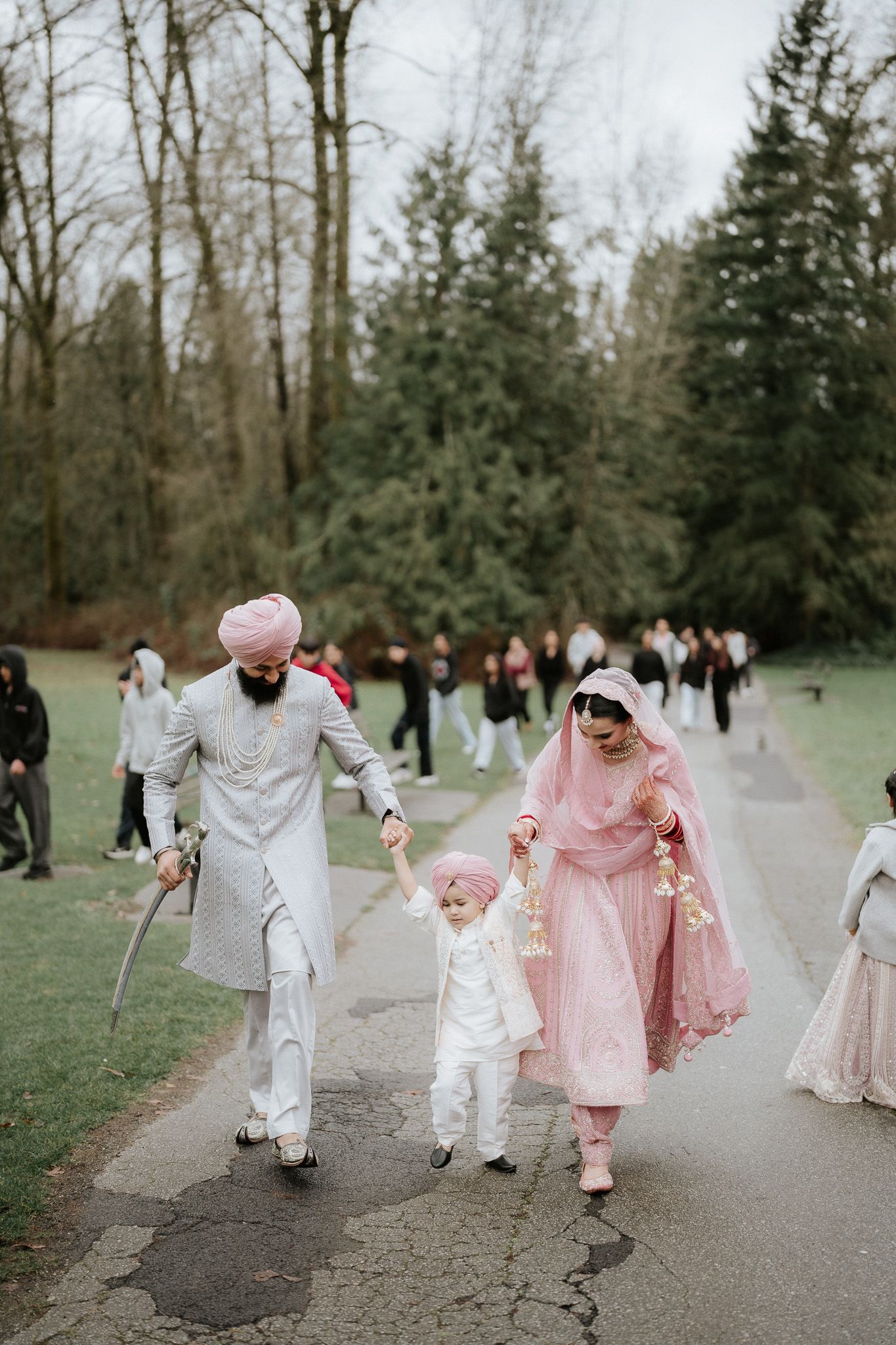 A family walking together on a path in a park wearing traditional white and pink cultural attire.