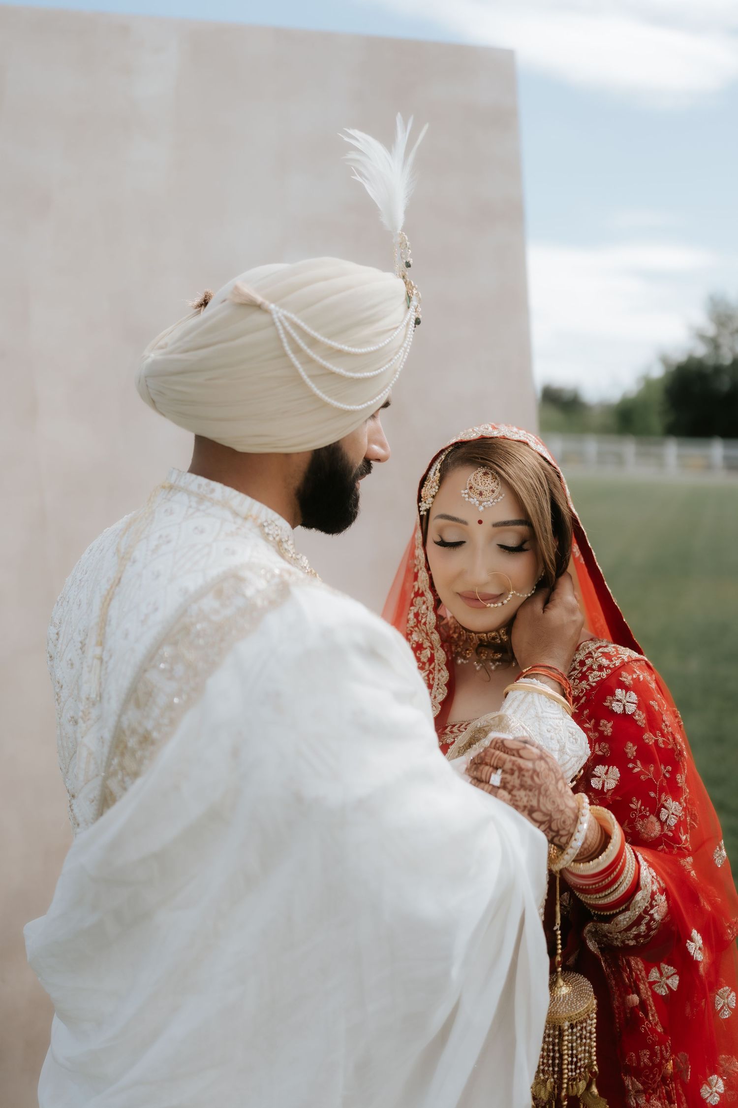 Sikh bride in red lehenga and groom in white sherwani and turban share an intimate moment at their wedding.