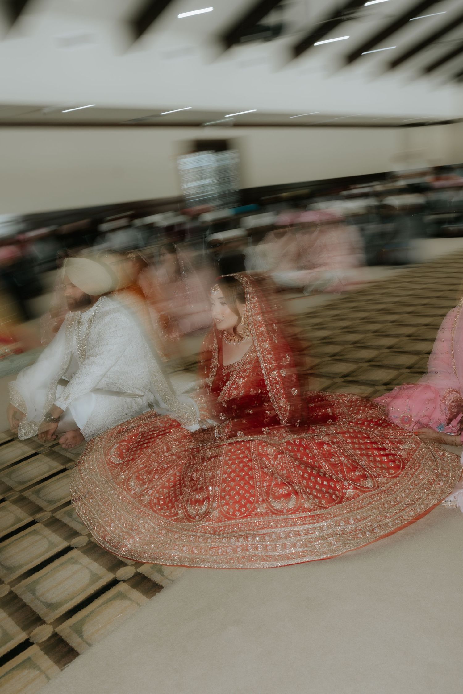 Blurred motion photo of Indian bride in red lehenga during Sikh wedding ceremony at a gurudwara.