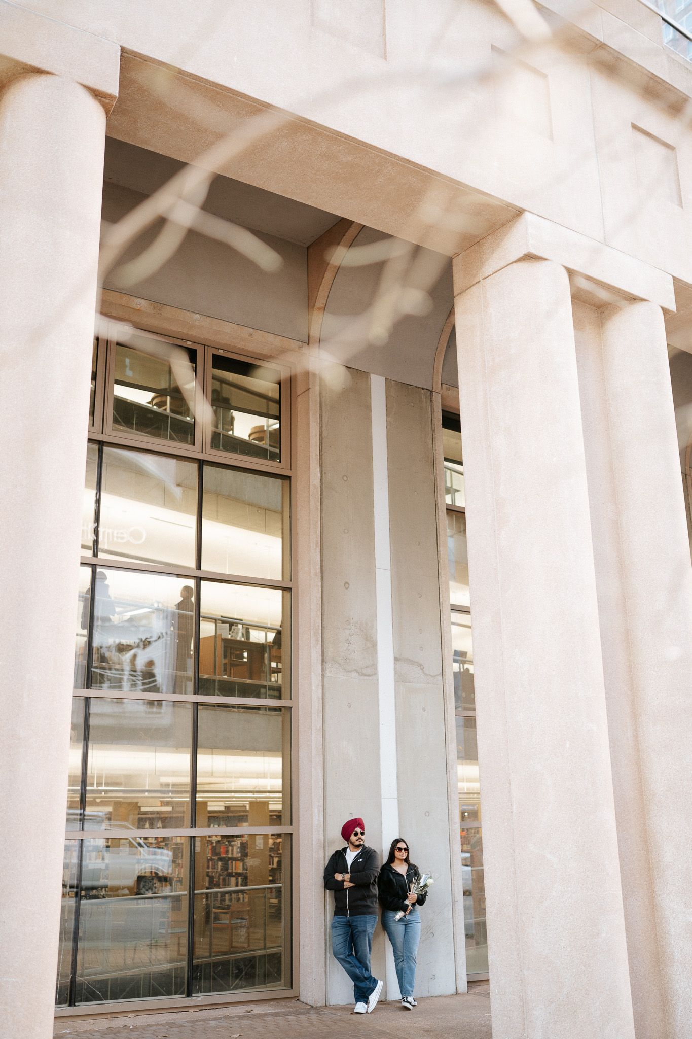 Modern building exterior features white columns and glass windows with people visible in the colonnade walkway.