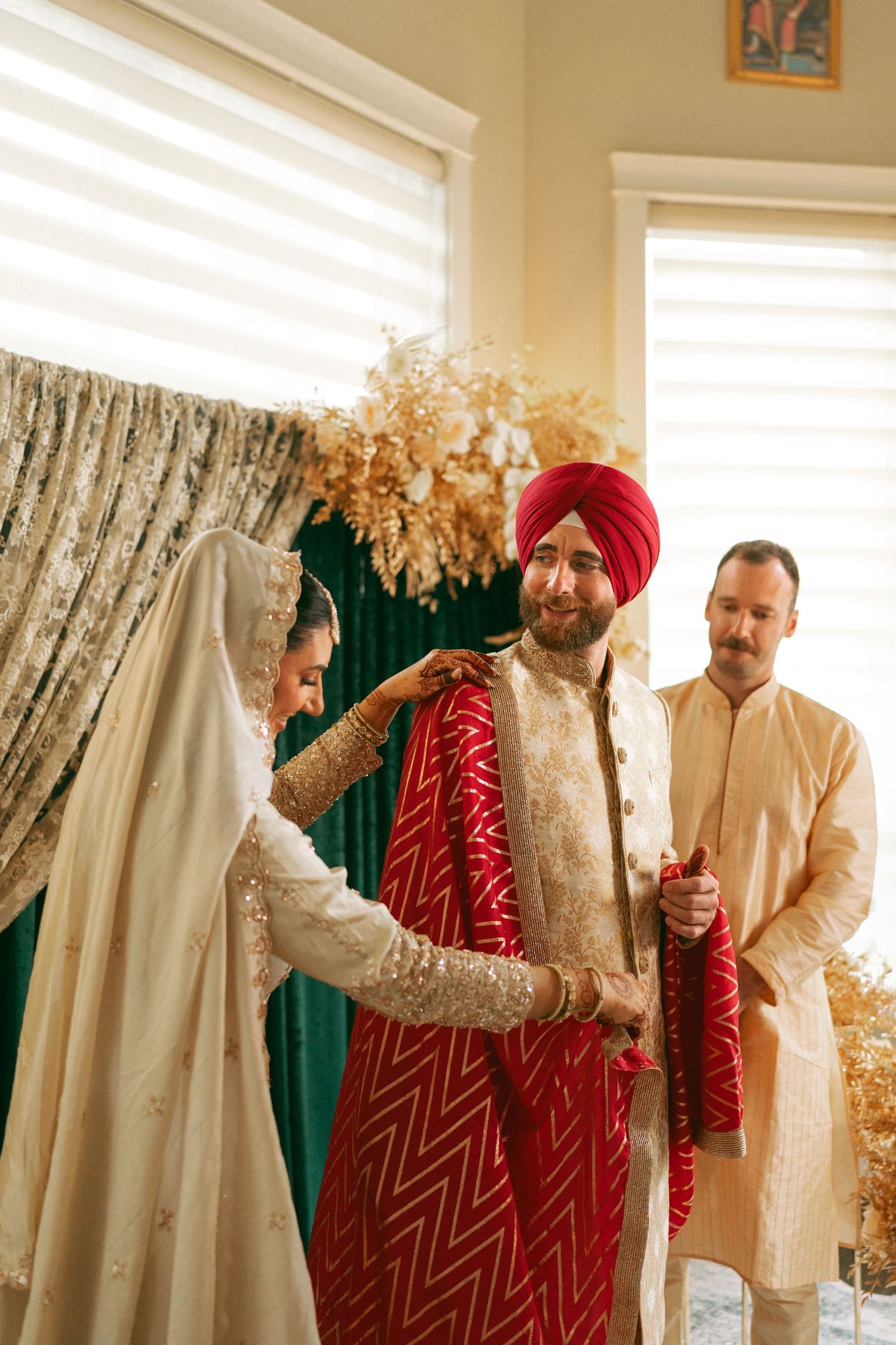 Sikh groom in red sherwani and turban during wedding ceremony with bride in embroidered white dupatta.