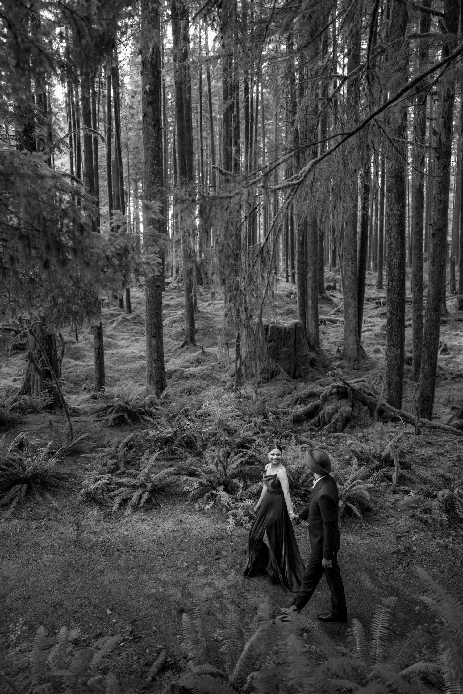 Black and white image of people walking through a moody forest landscape.