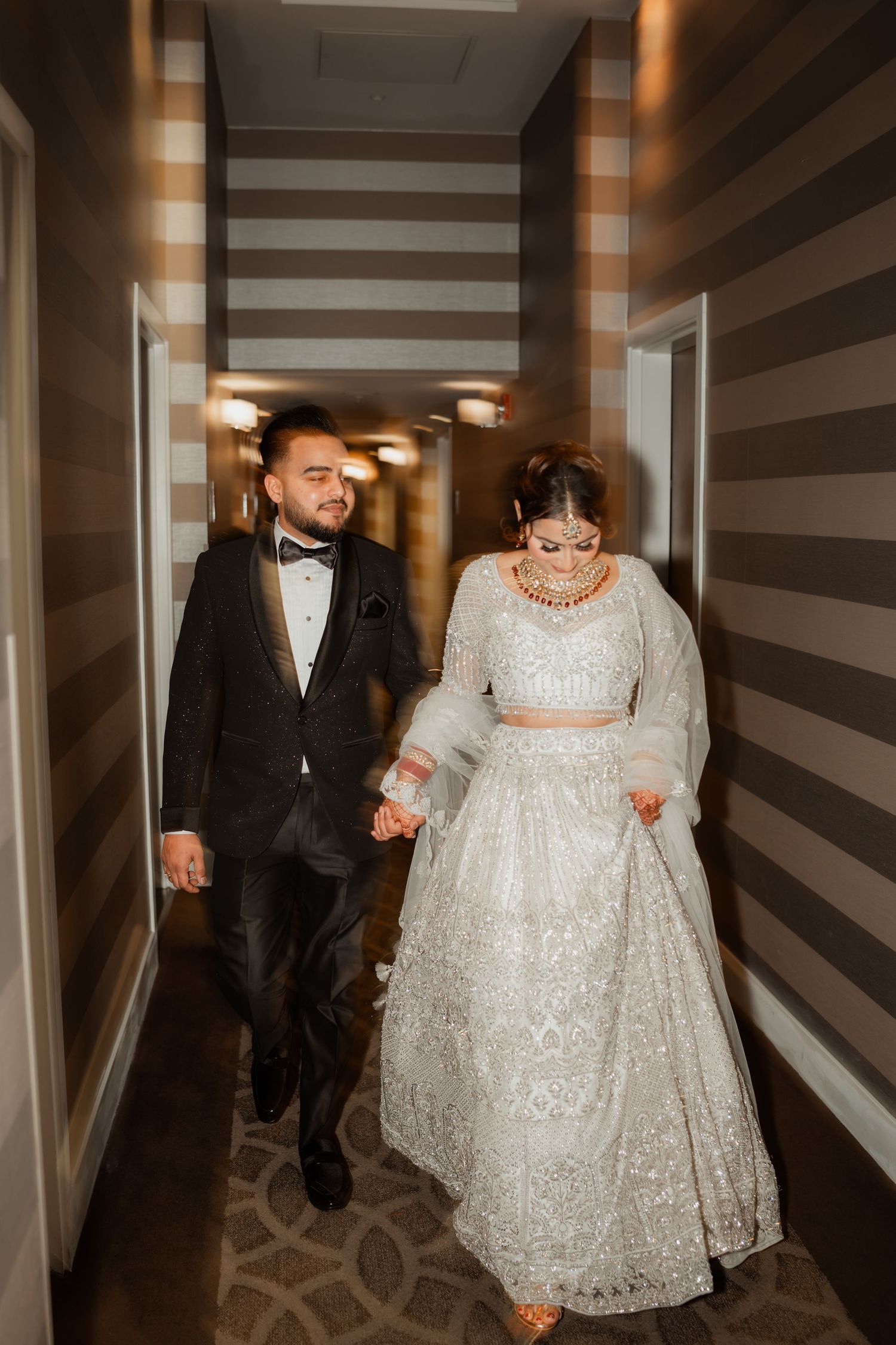 A couple walks hand in hand down a modern hotel corridor.