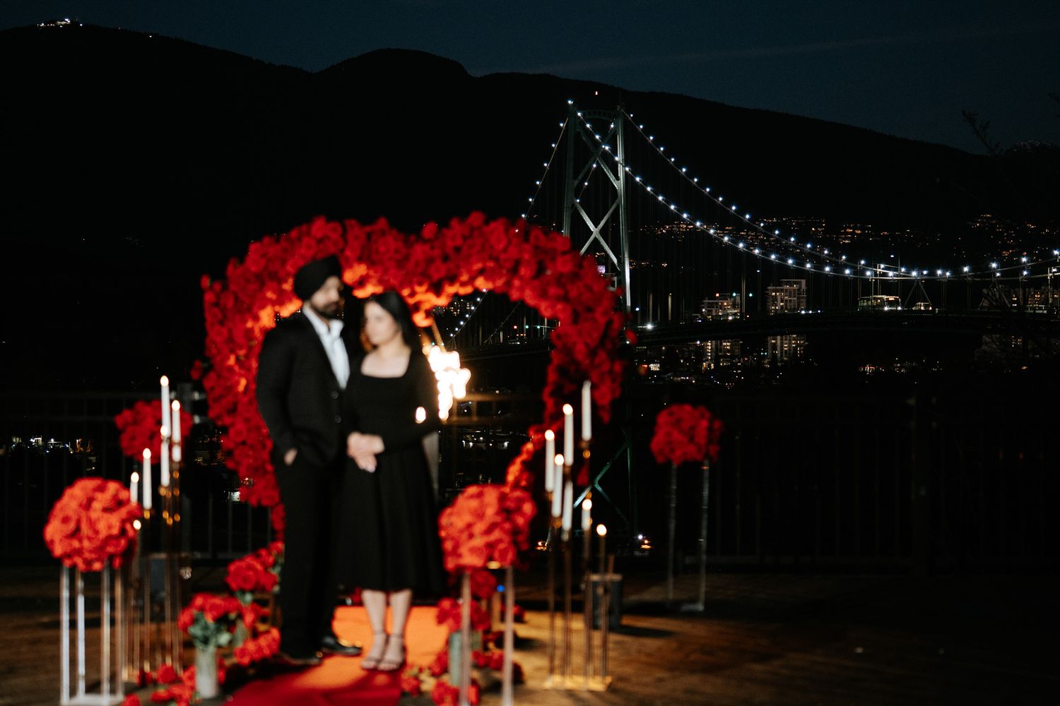 Outdoor evening wedding reception with red floral arrangements and string lights creating a romantic ambiance.