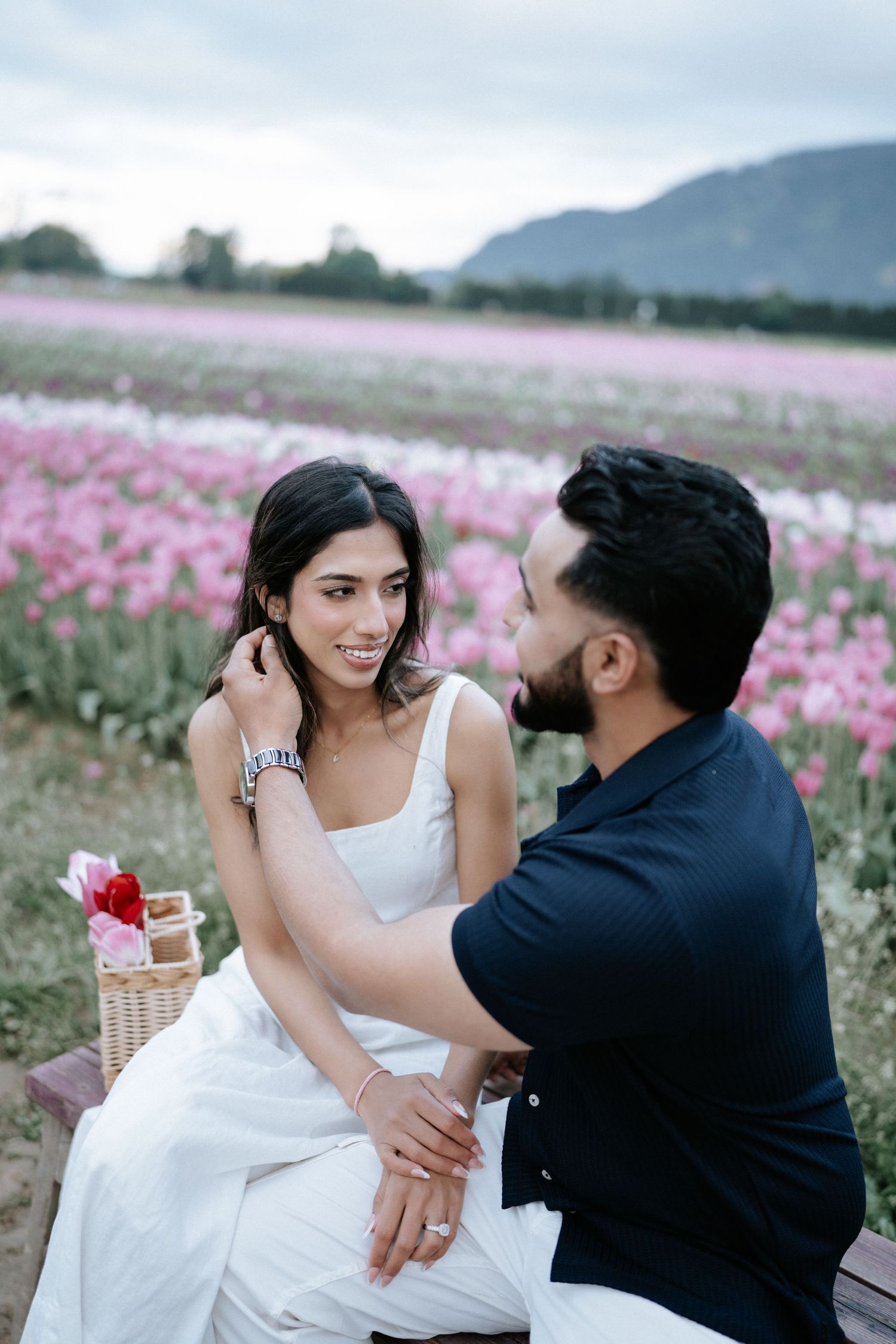 A couple shares romantic moments together in a blooming pink flower field on a cloudy day.