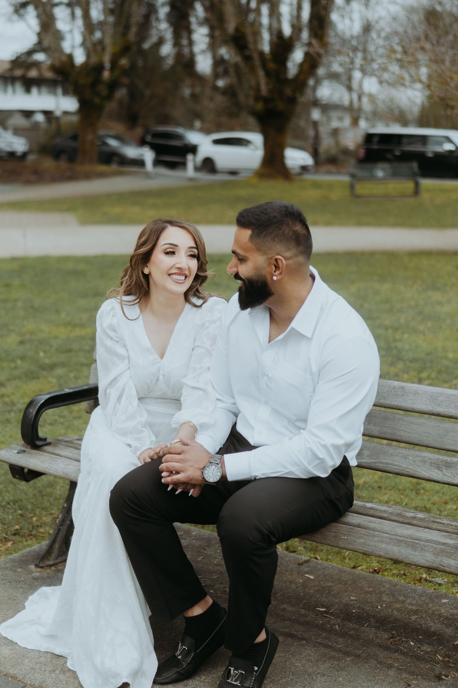Two people in white shirts share intimate moments while sitting on a park bench on an overcast day.