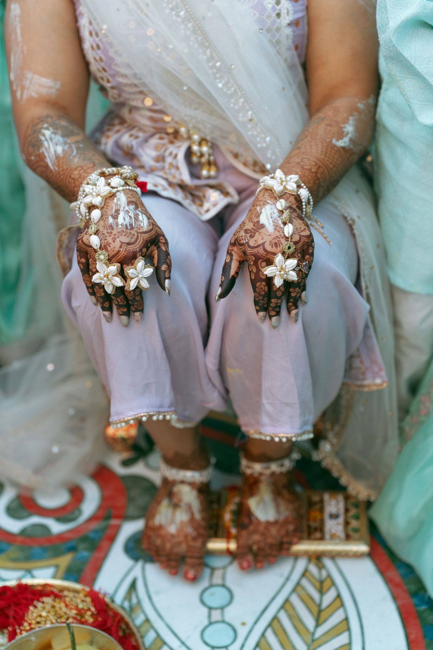 Indian bride displaying intricate henna mehndi designs on hands adorned with white floral jewelry during wedding ceremony.