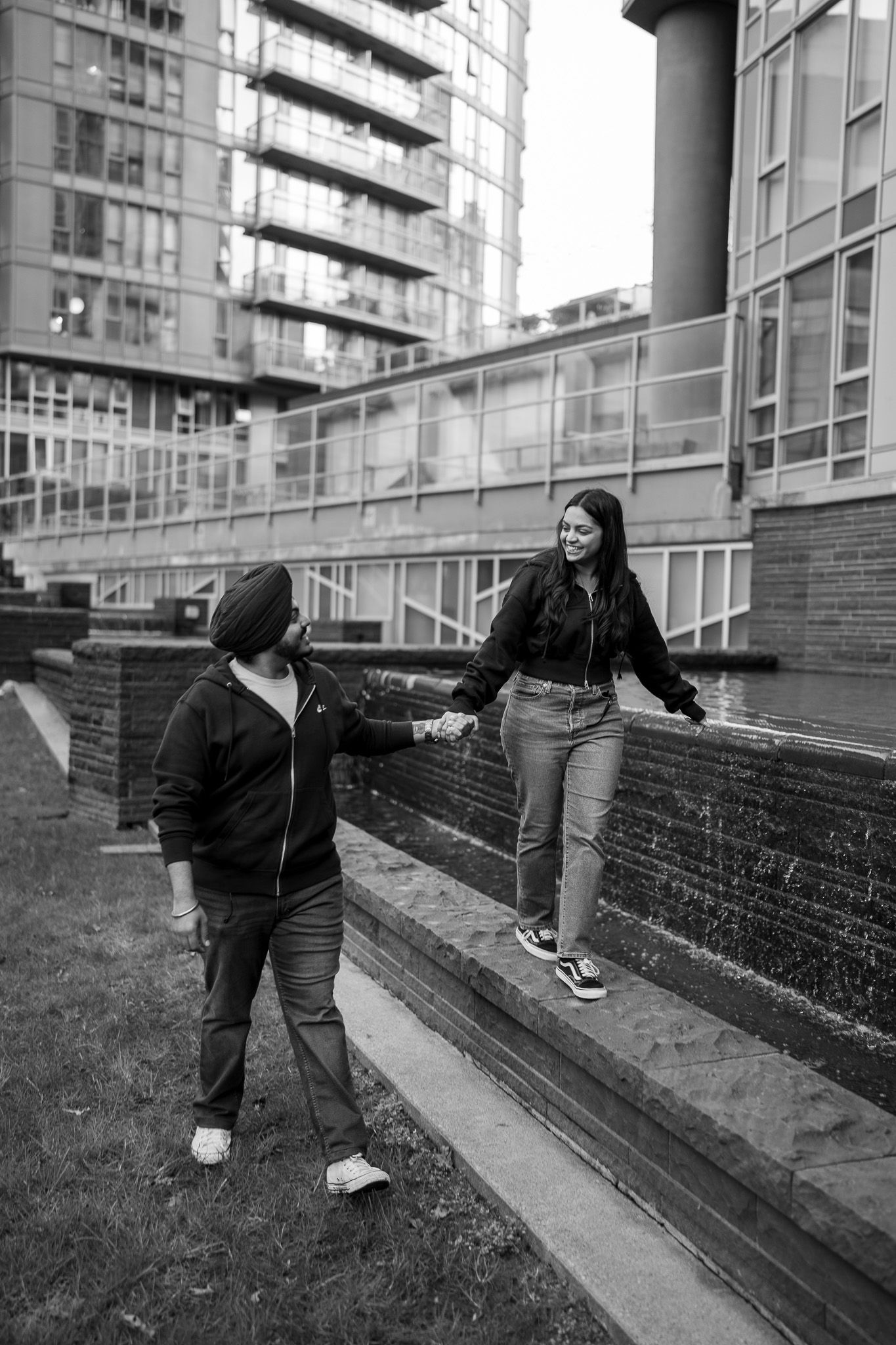 A sequence of four black and white photos showing playful movements along an urban brick wall with grass.