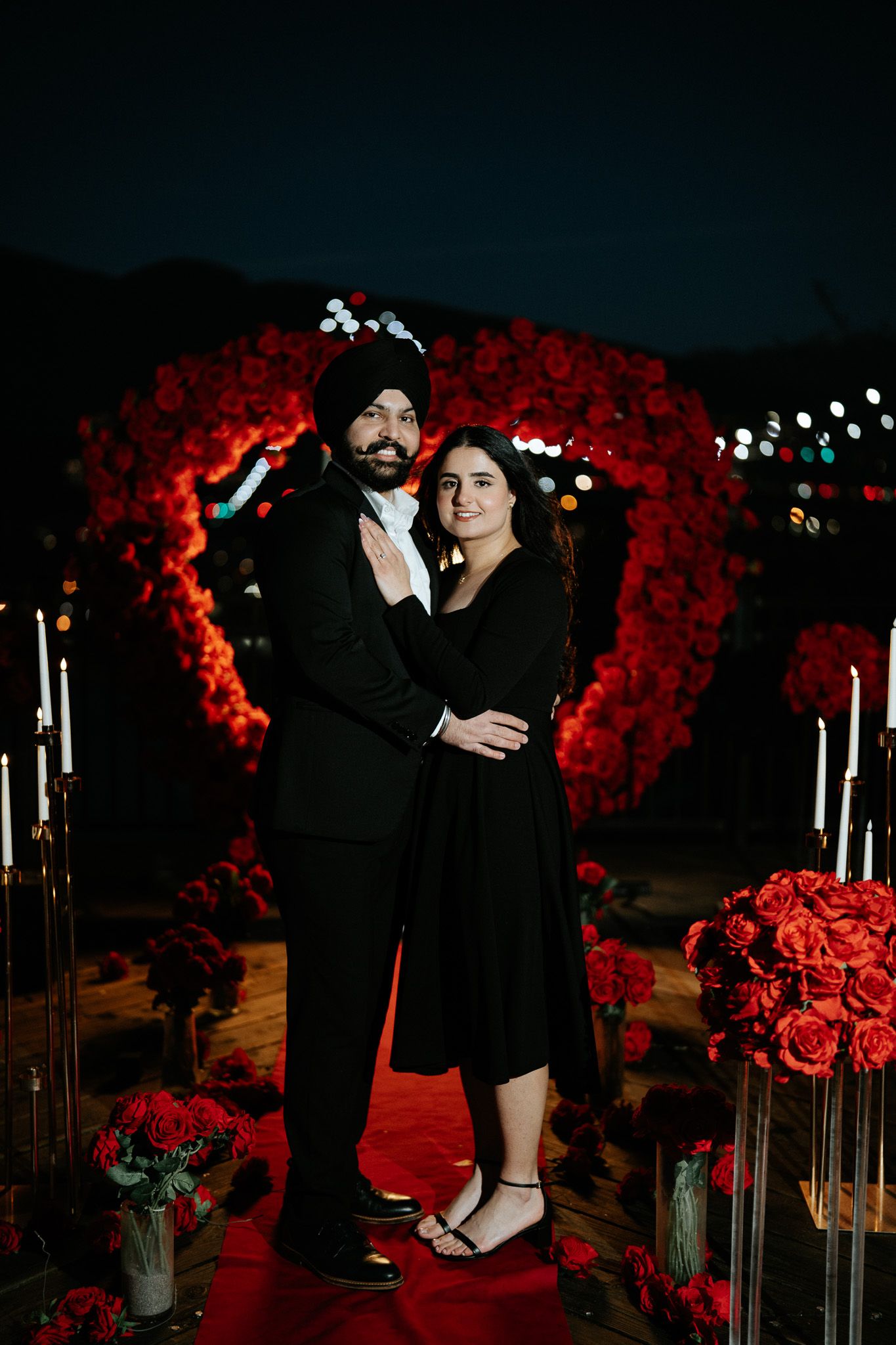 A romantic couple dancing together in front of a backdrop of red roses and candlelight in an elegant setting.