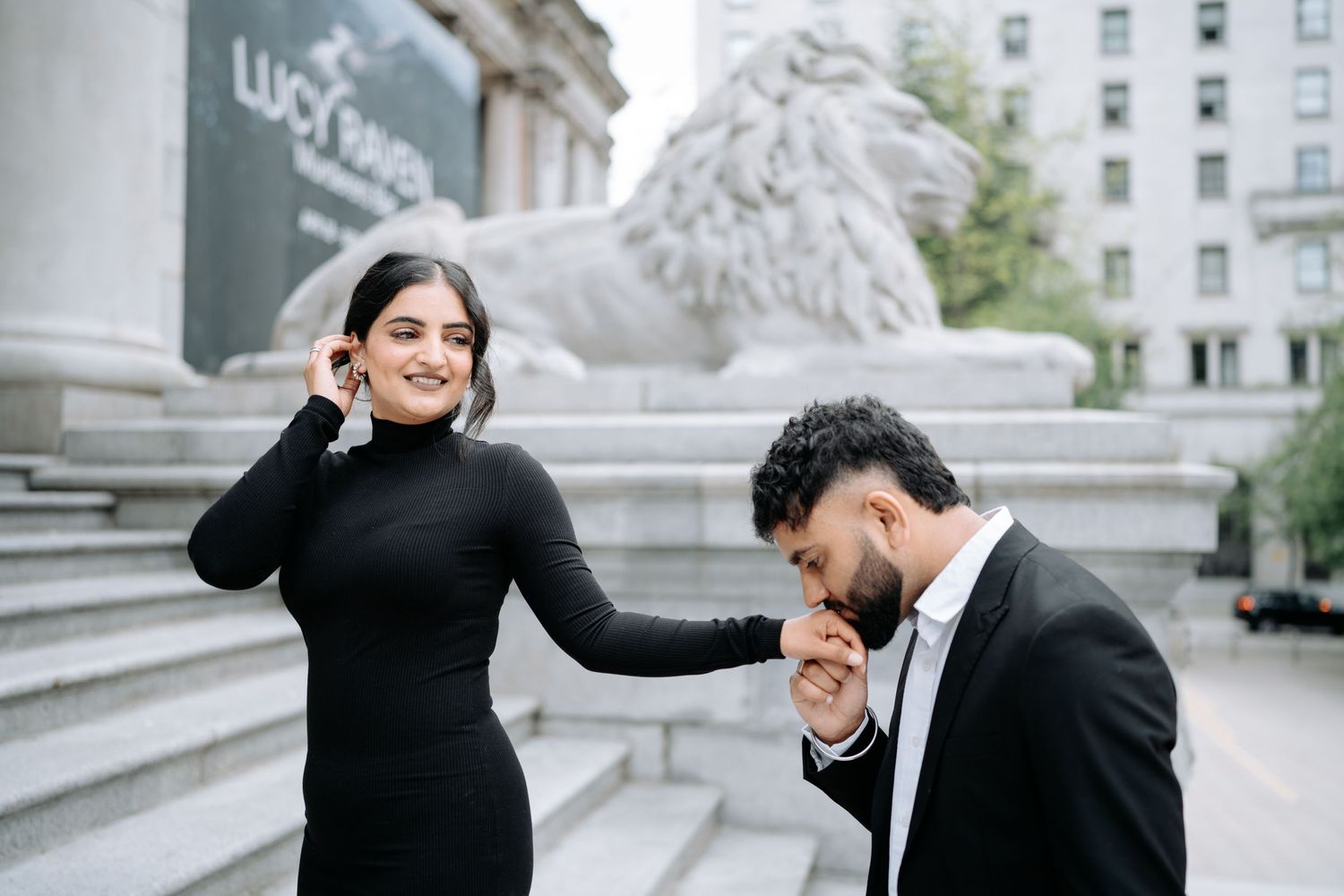 A couple shares intimate moments on the steps of a classical building with stone lions.