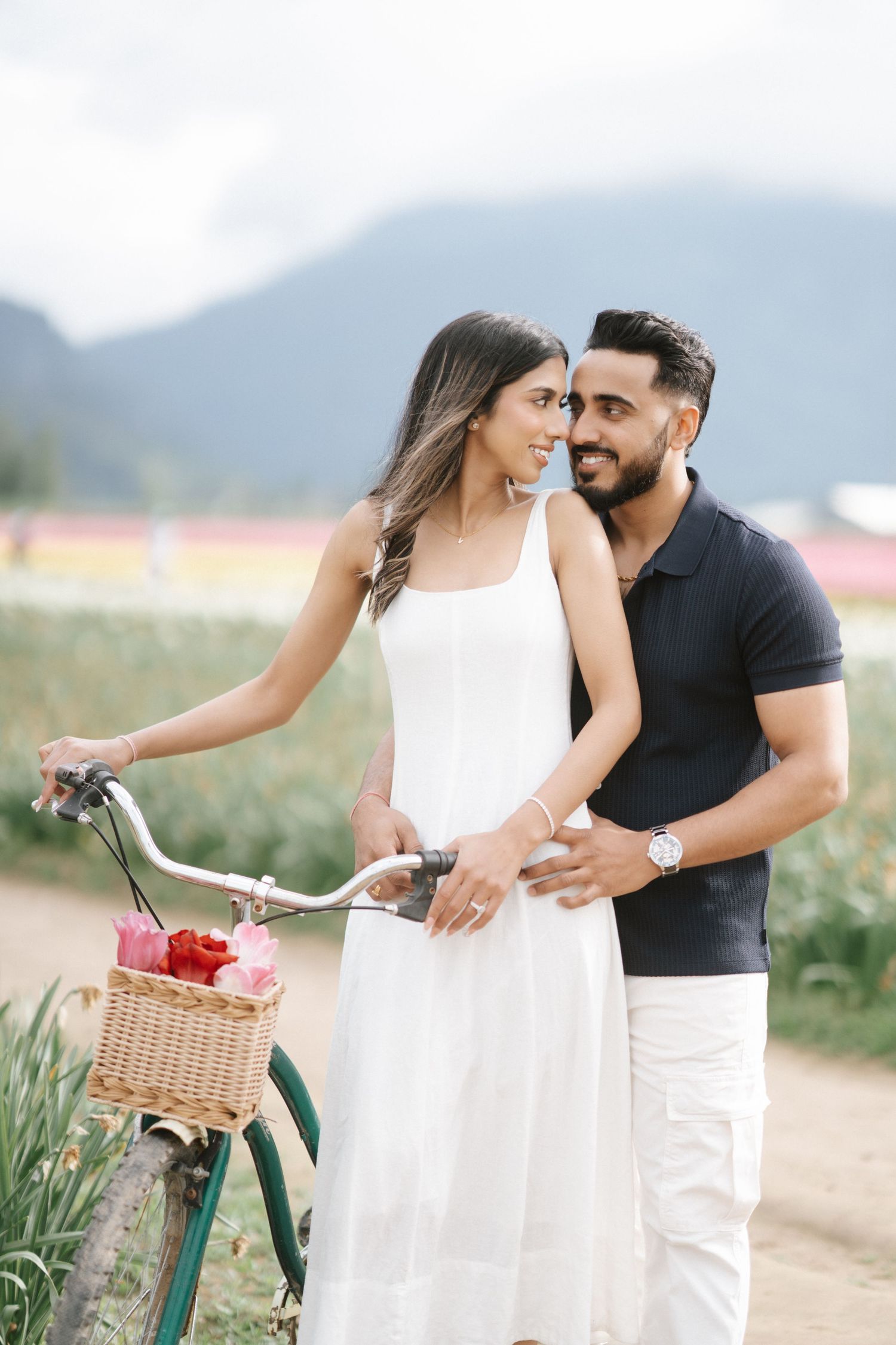 A couple shares a romantic moment outdoors with a vintage bicycle adorned with a basket of flowers.