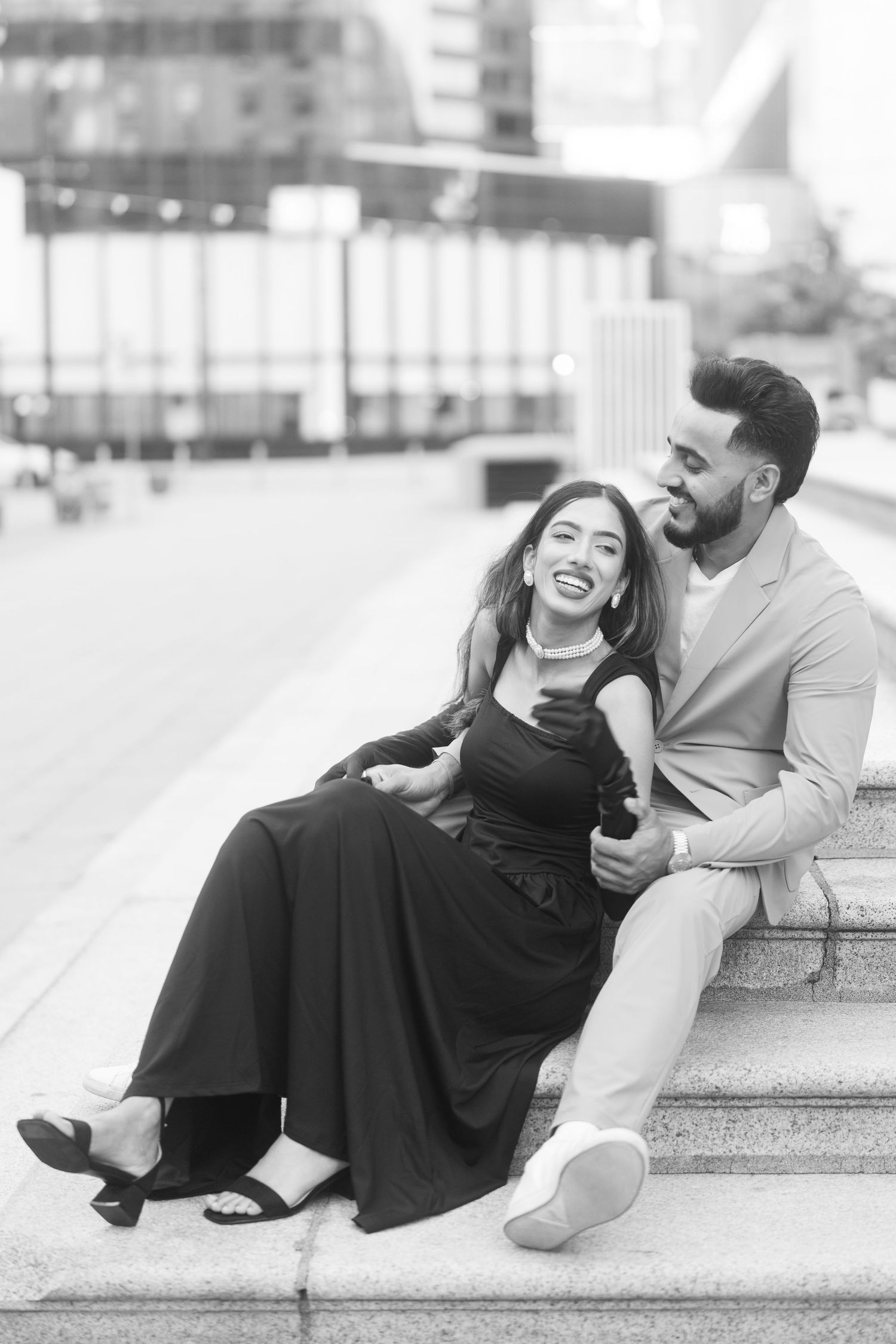 A couple shares a joyful candid moment while sitting on outdoor steps in black and white photography.