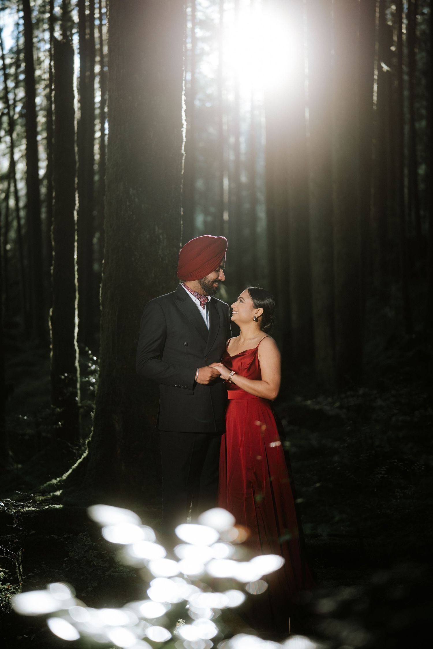 Forest engagement session with sunlit ground and towering pine trees in background.