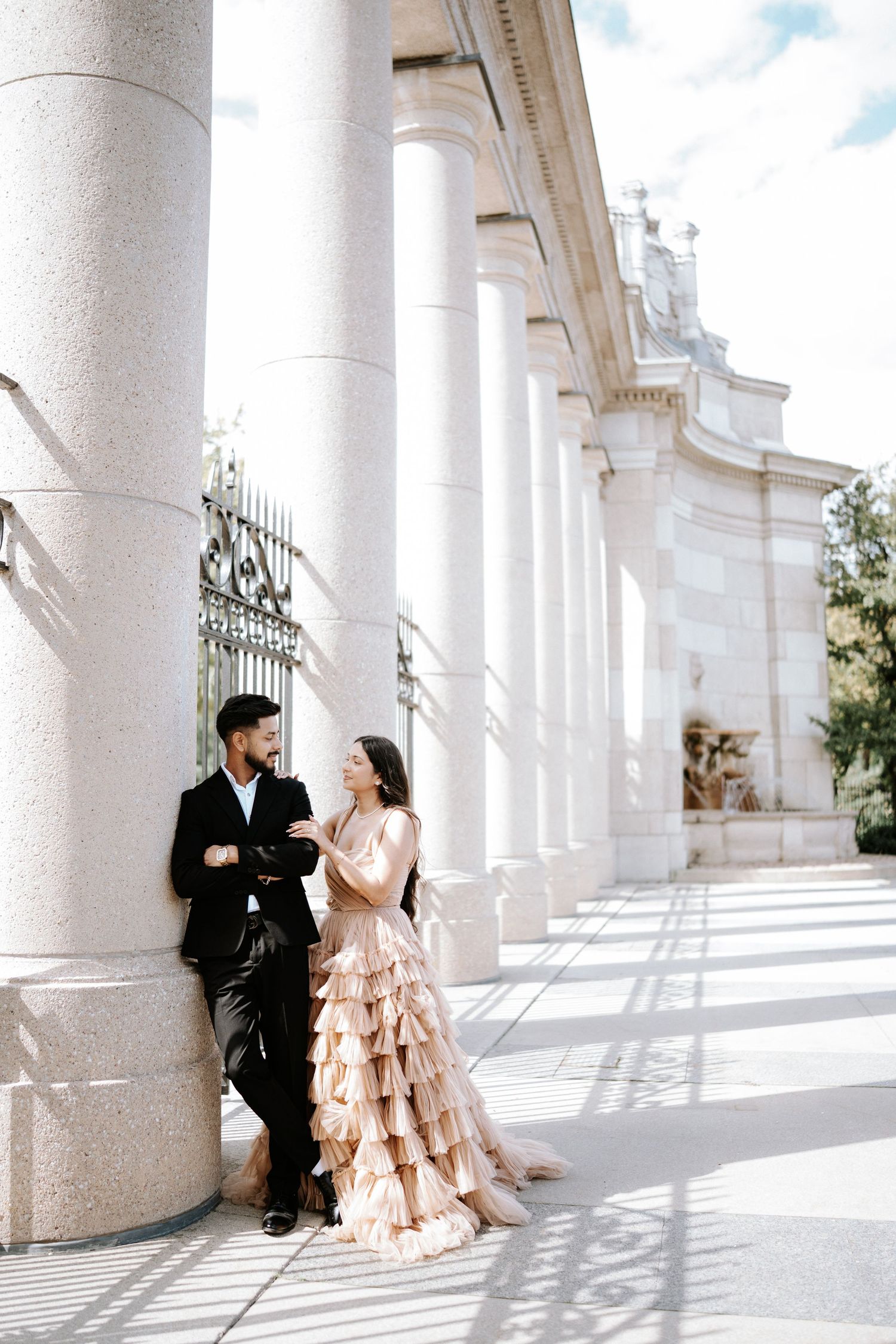 Elegant couple poses in a bright colonnade with white pillars and romantic lighting.