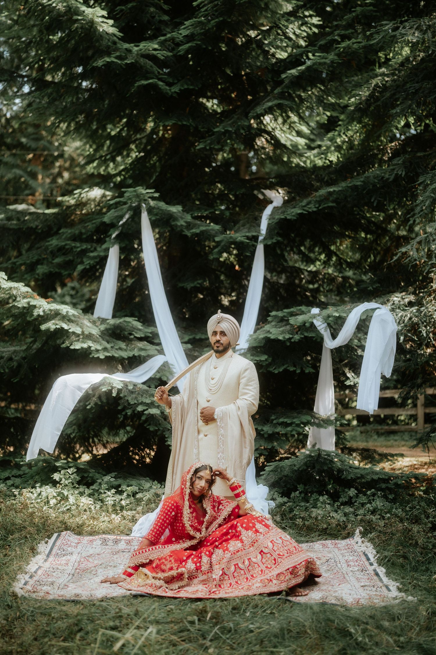 Outdoor wedding photoshoot in a forest setting with white fabric decorations and traditional attire.
