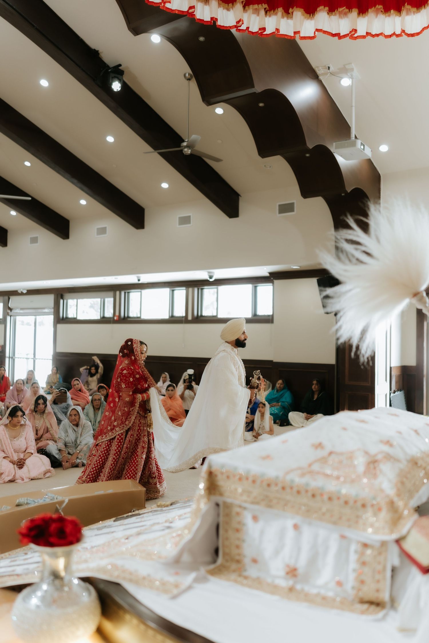 Sikh wedding ceremony with bride in red lehenga and groom in white completing Anand Karaj rituals around the Guru Granth Sahib.