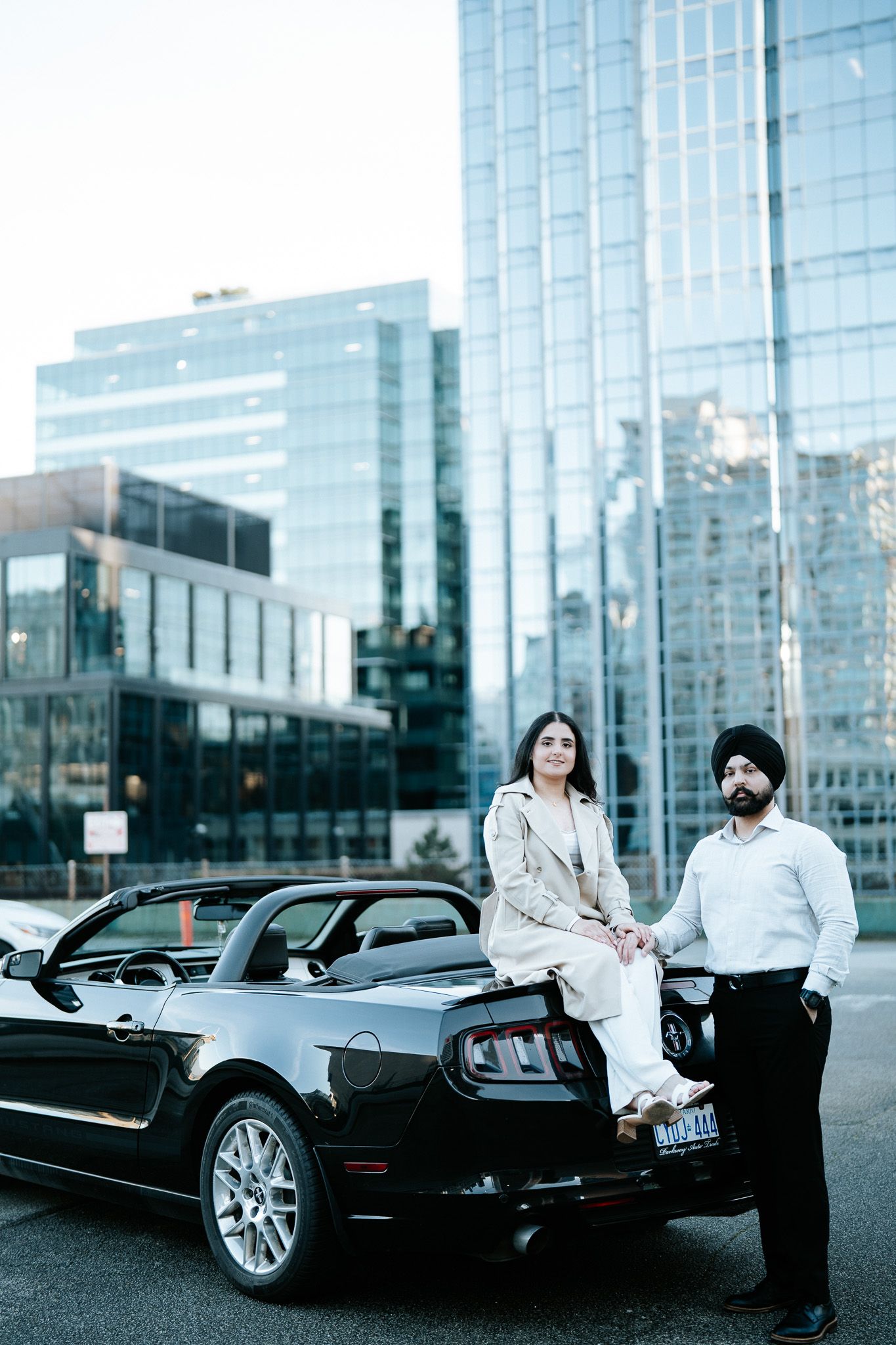 Business professionals stand near a luxury black convertible car outside a modern glass office building.