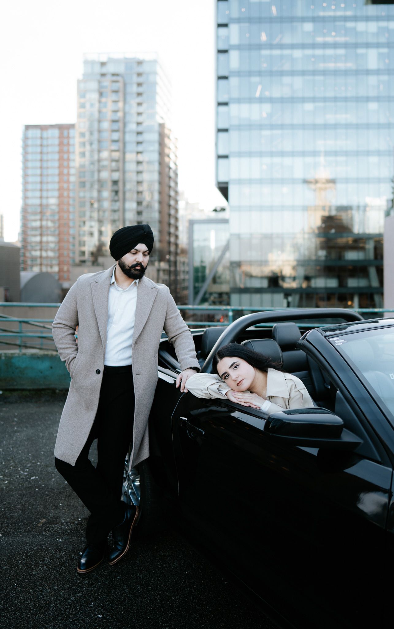 A person in a grey blazer interacting with a parked black luxury car in an urban setting.