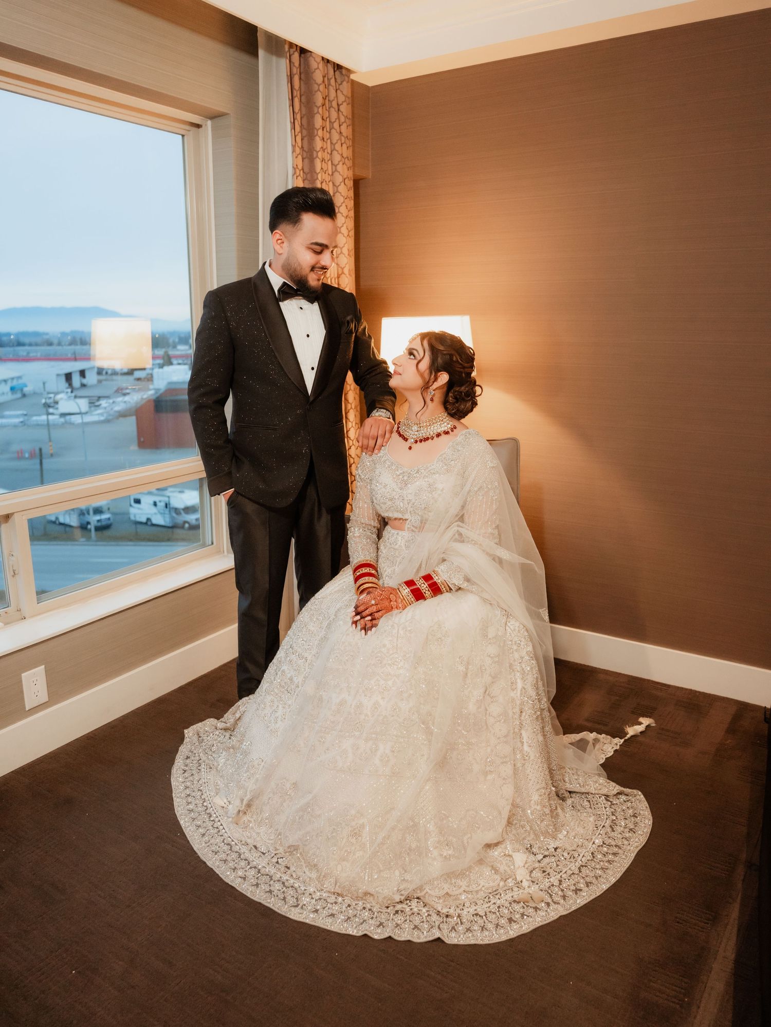 A couple sits together on dark hardwood flooring in formal attire.