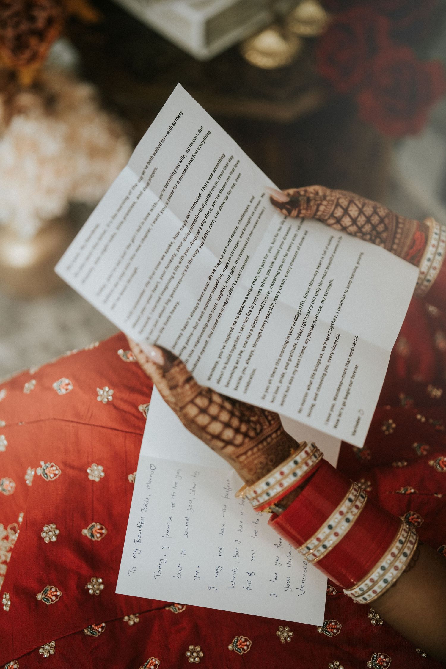 Close-up of handwritten wedding vows or letters with red traditional Indian bridal attire in background.