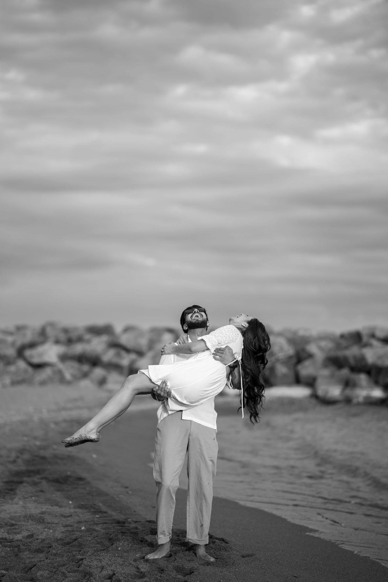 A playful dance lift sequence on a beach with rocks and cloudy skies in the background.