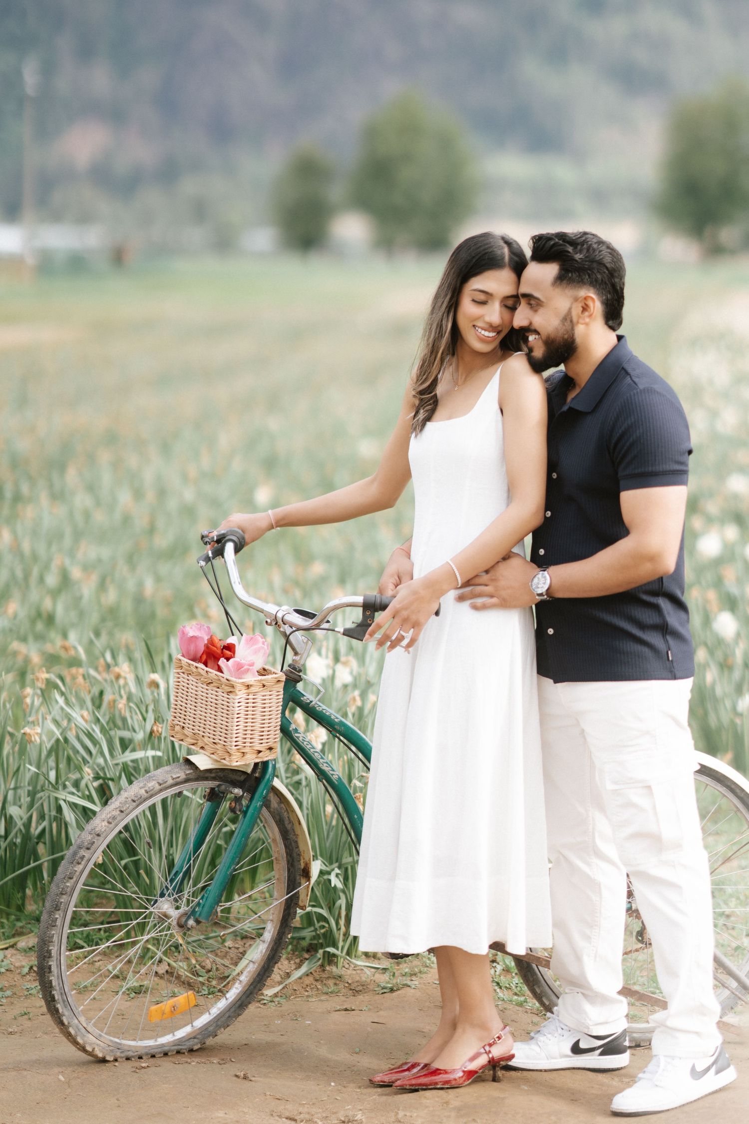 A romantic couple poses with a vintage green bicycle in a scenic pineapple field during a tropical photoshoot.