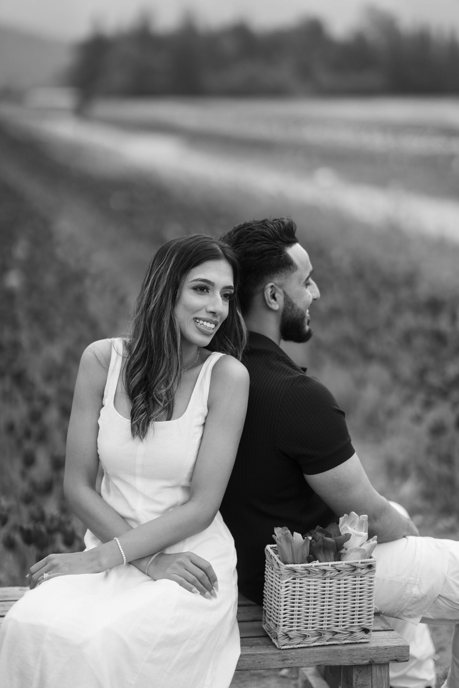 A couple enjoys a romantic black and white picnic scene together in a meadow with a white wicker basket.