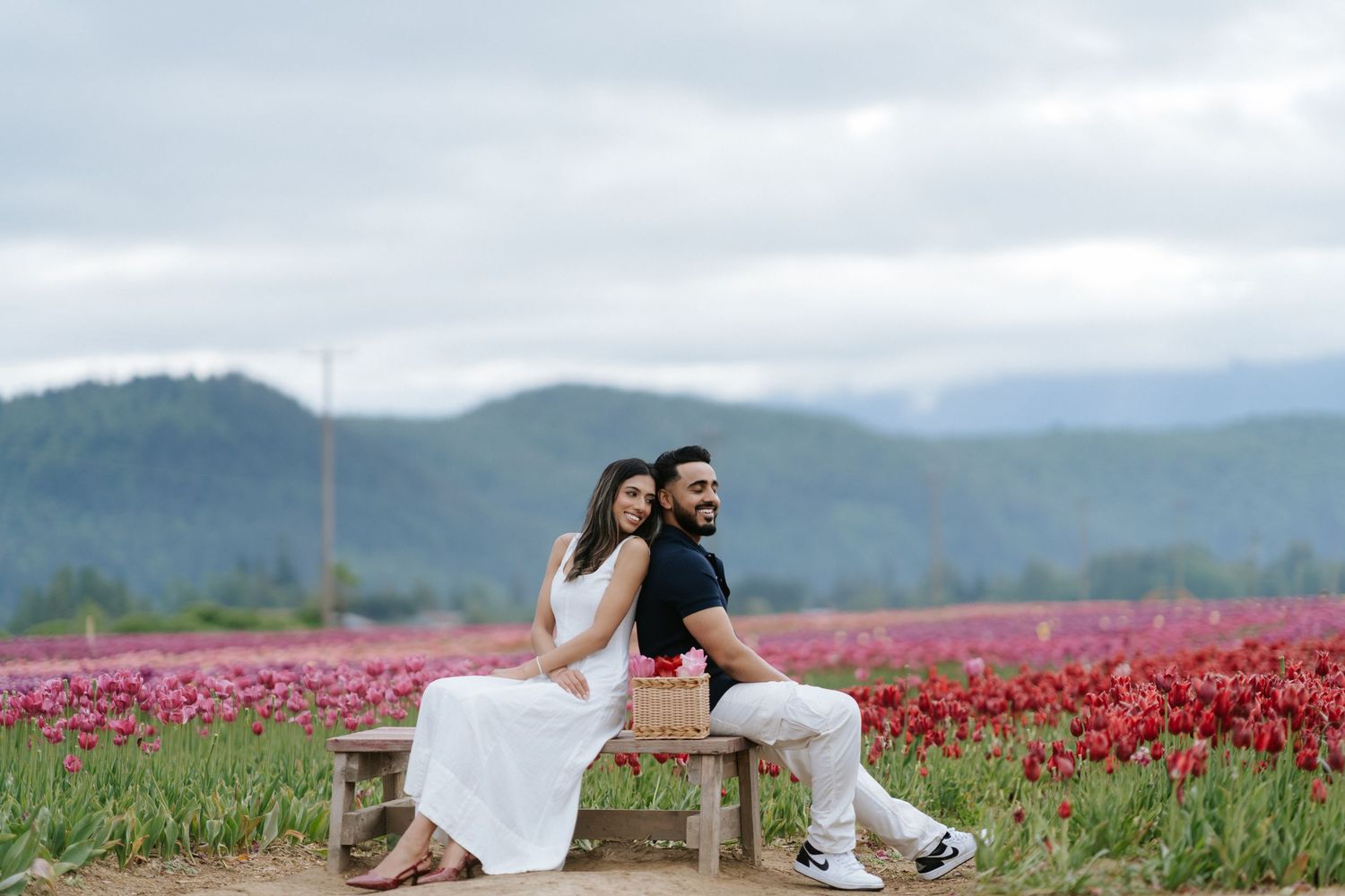 Couple posing in a vibrant pink tulip field with mountains in the background during sunset.