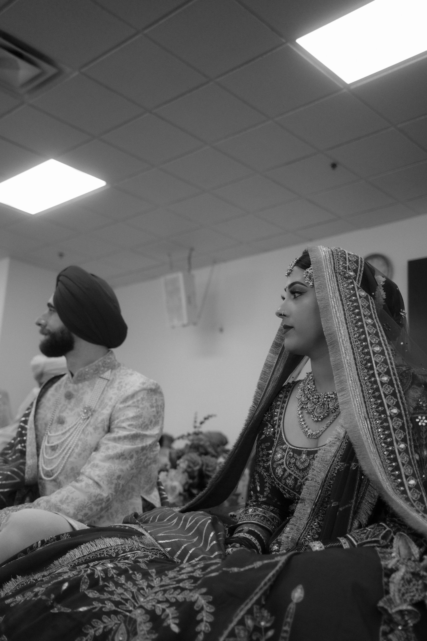 Black and white photo of a Sikh bride and groom in traditional wedding attire during a ceremony.