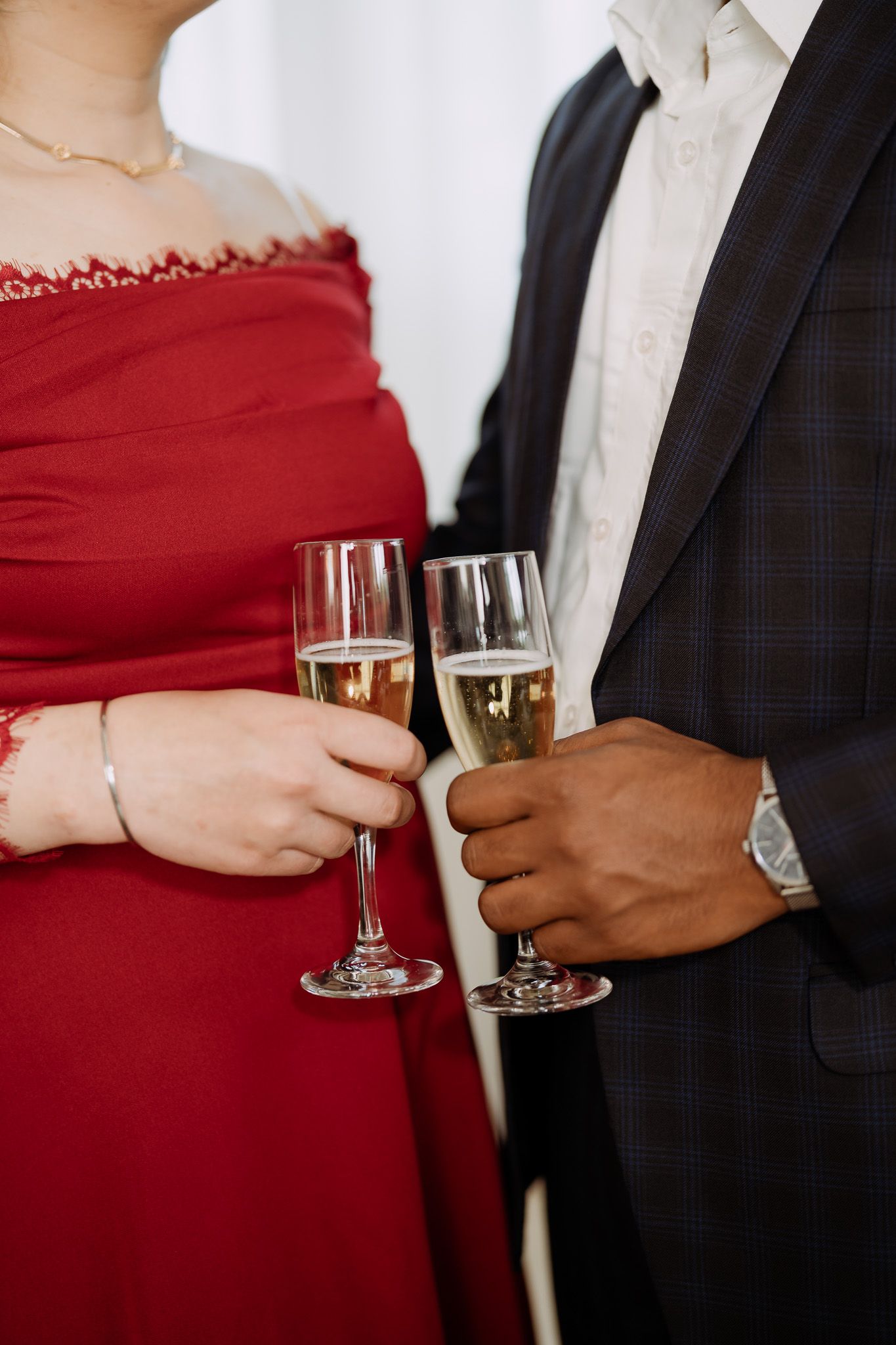Interracial couple toasting with champagne glasses at a formal event, woman in red dress, man in plaid suit.