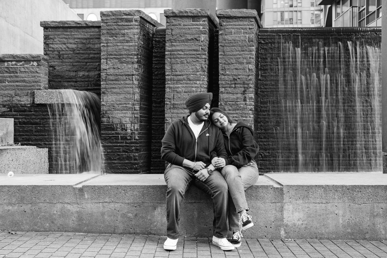A black and white panoramic street scene shows two people walking past a brick wall in an urban setting.