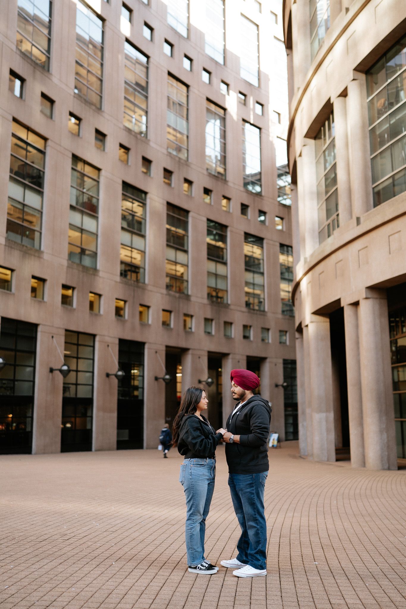 People stand in a modern courtyard surrounded by tall brown buildings with curved architecture and large windows.