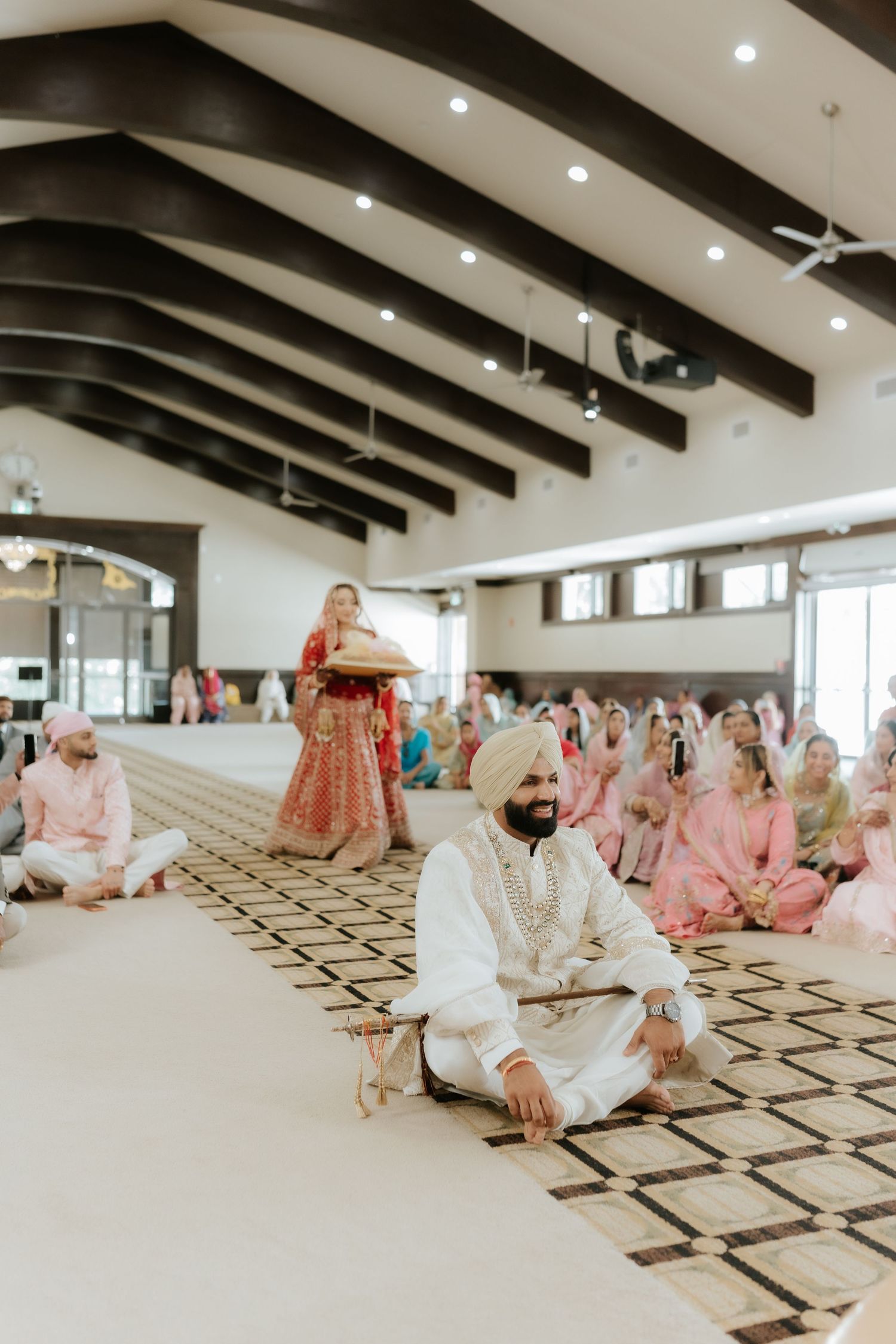 Sikh groom in white sherwani and turban seated during traditional Anand Karaj wedding ceremony in elegant hall.