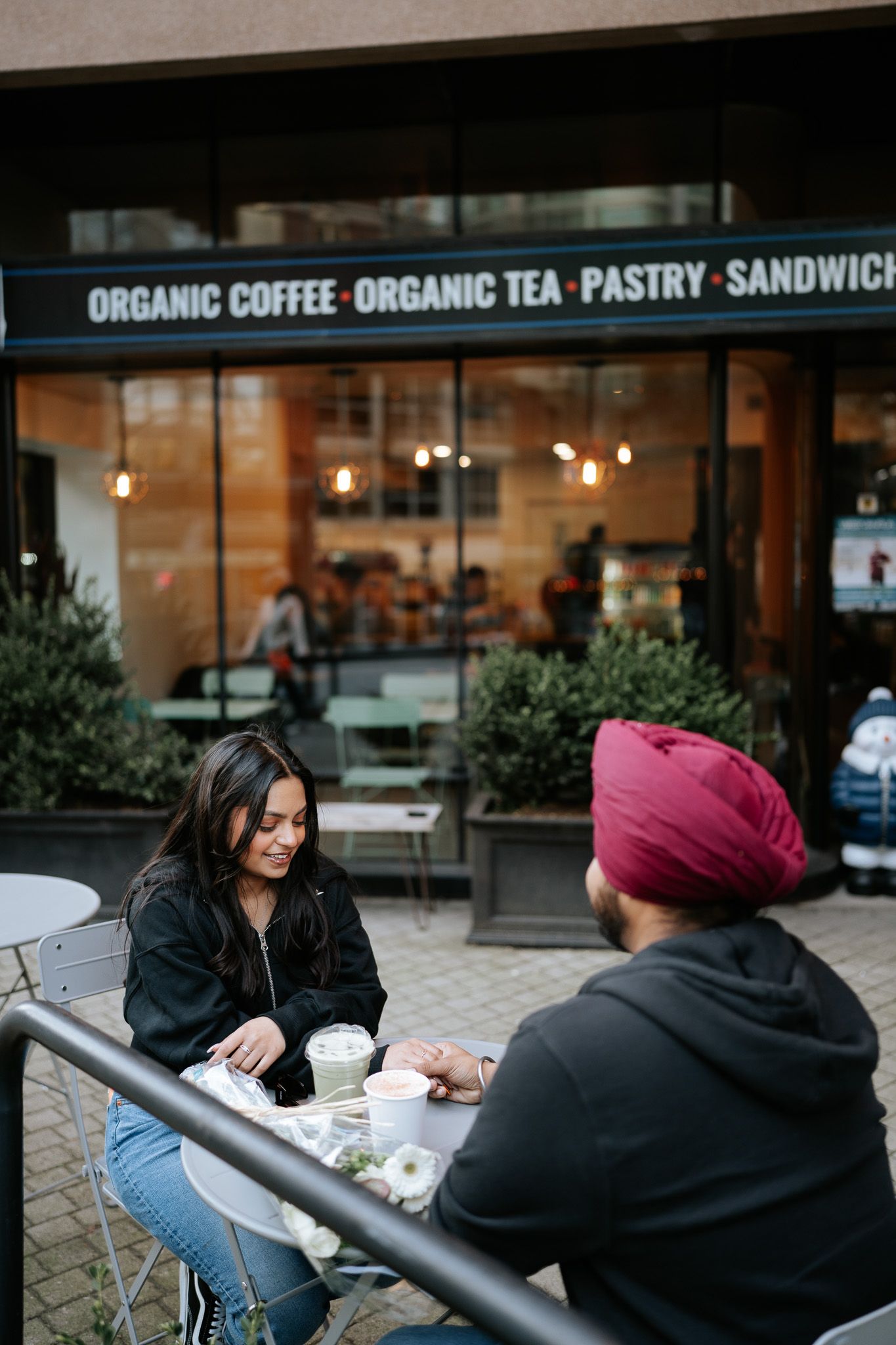 Friends having a casual conversation while seated at outdoor tables near a coffee shop.