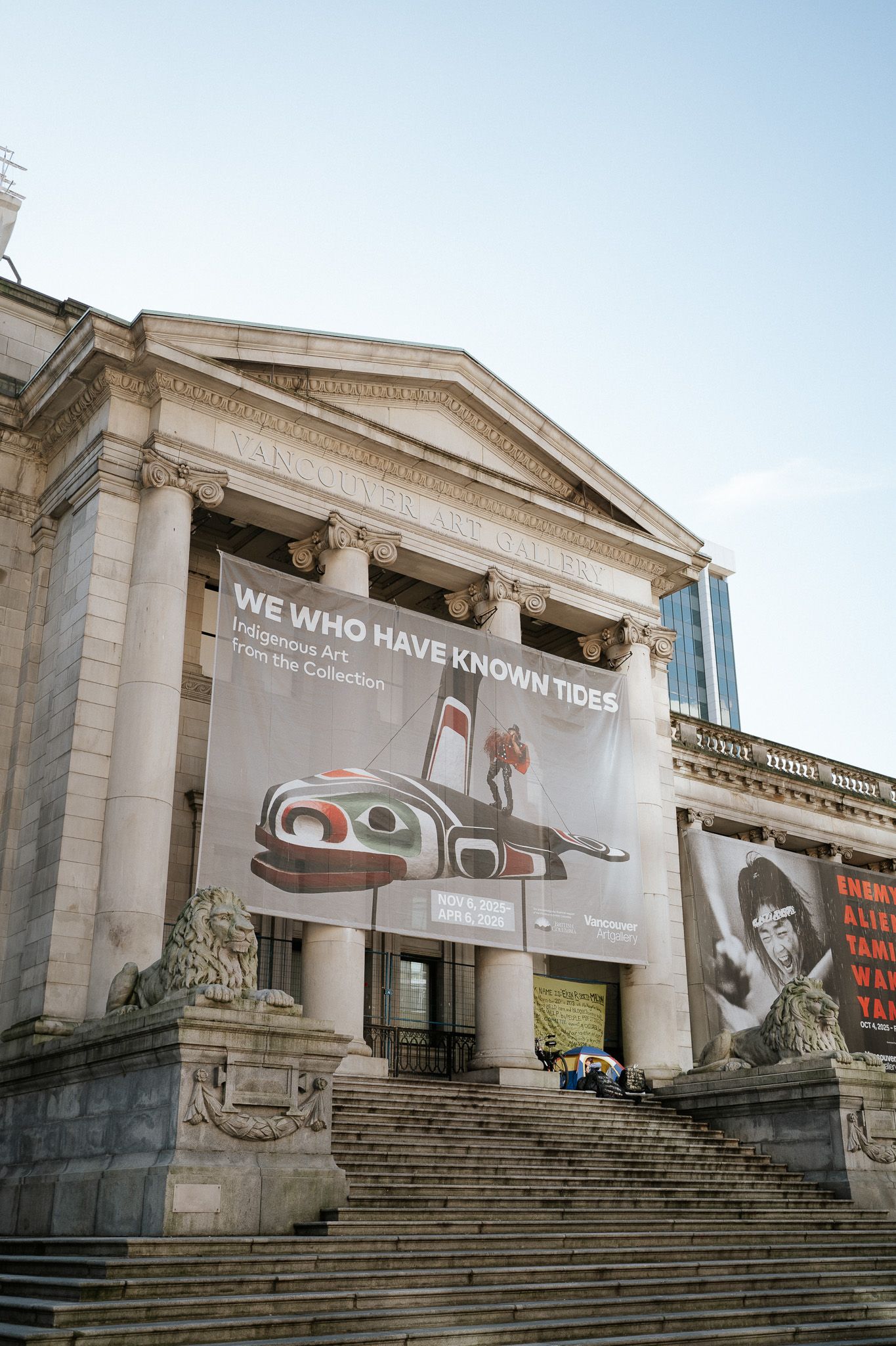 Grand stone building with classical columns displaying a large banner for 'We Who Have Known These' exhibition on its facade.