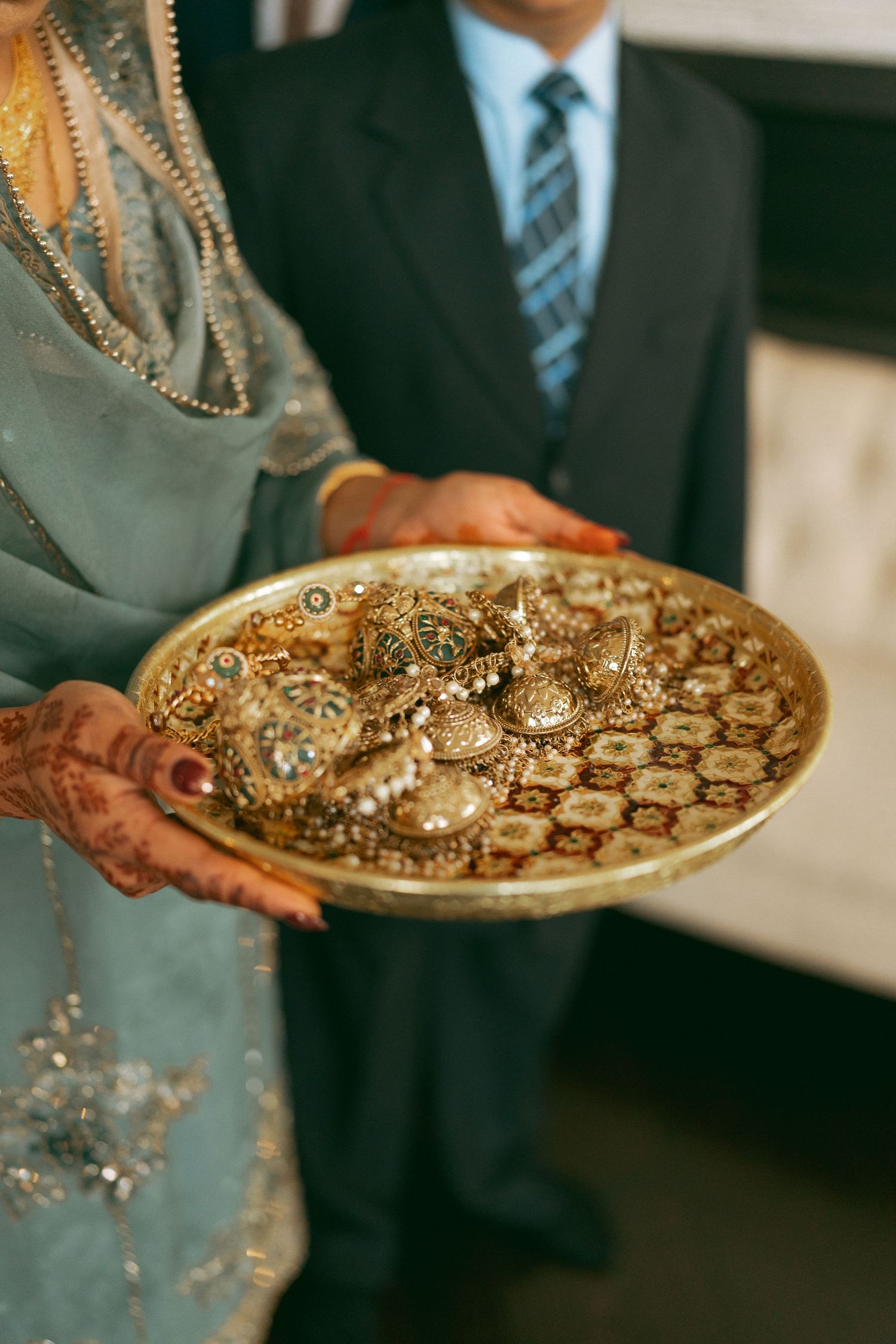 Bride and groom holding a golden thali plate with traditional Indian bridal jewelry at a wedding ceremony.