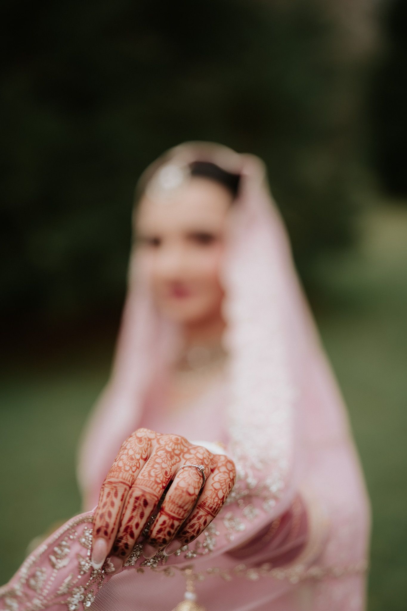 Close-up view of henna-decorated hands with intricate patterns against a pink traditional dress background.
