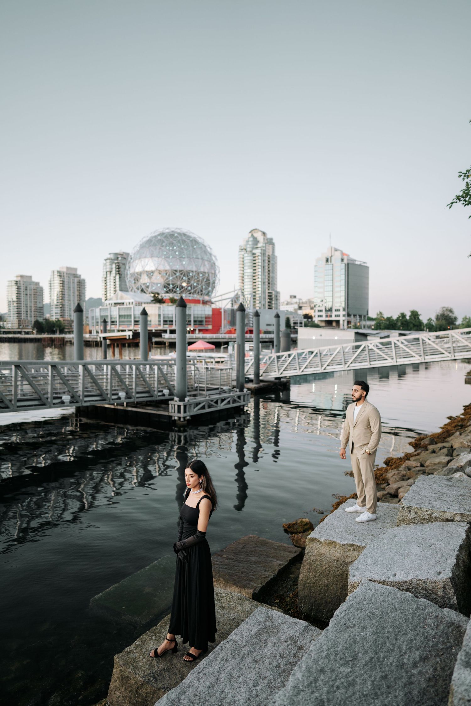 Two people pose along the waterfront in Vancouver with Science World and city skyline visible in background.