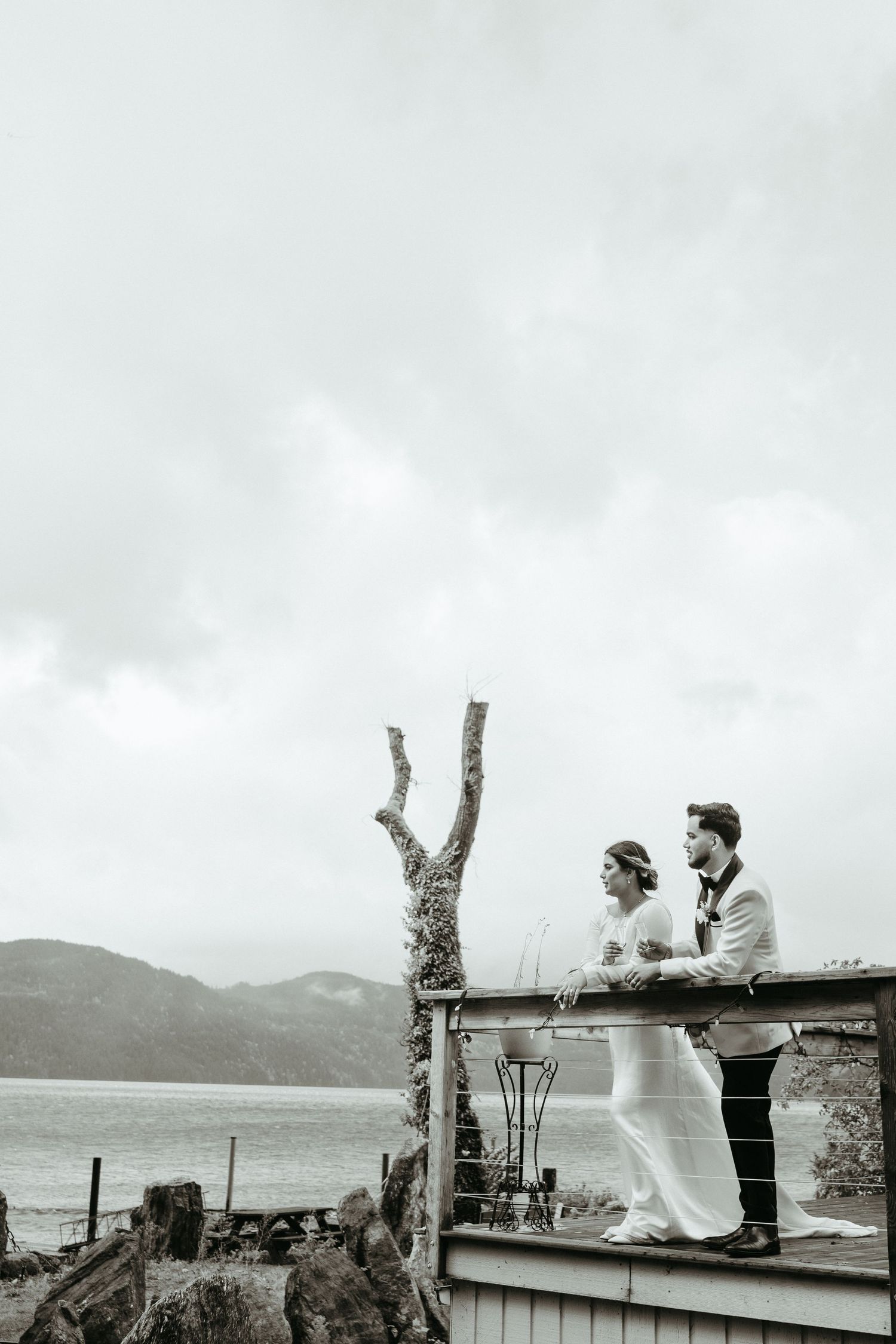 A series of black and white photos showing a couple sitting on a railing by the ocean with mountains in the background.